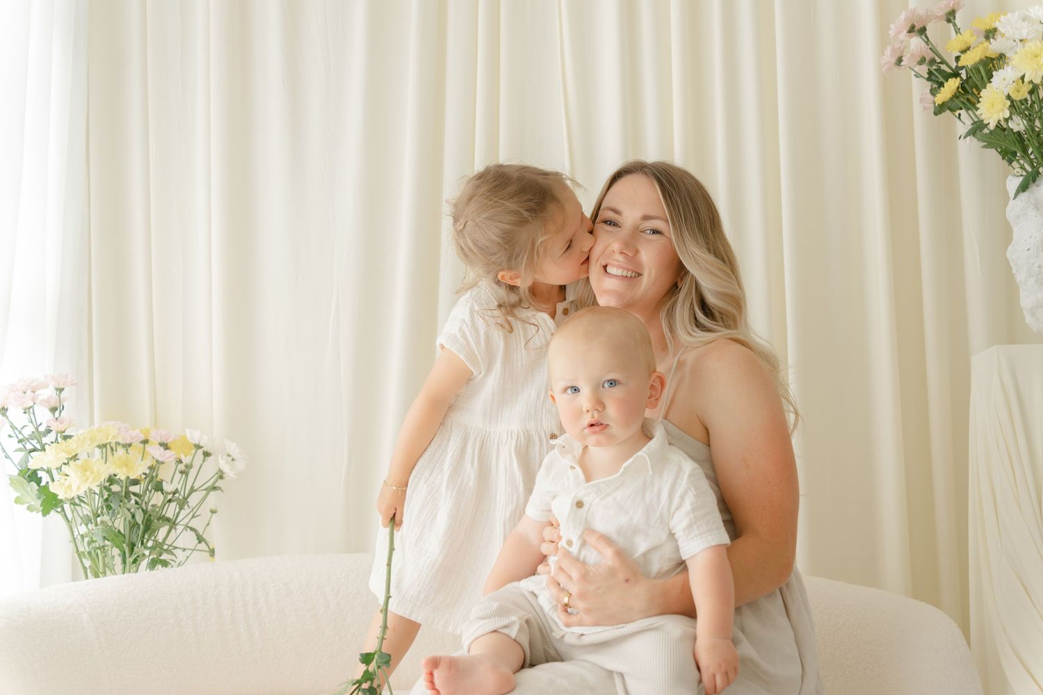A joyful family portrait against white curtains with fresh flowers in the background