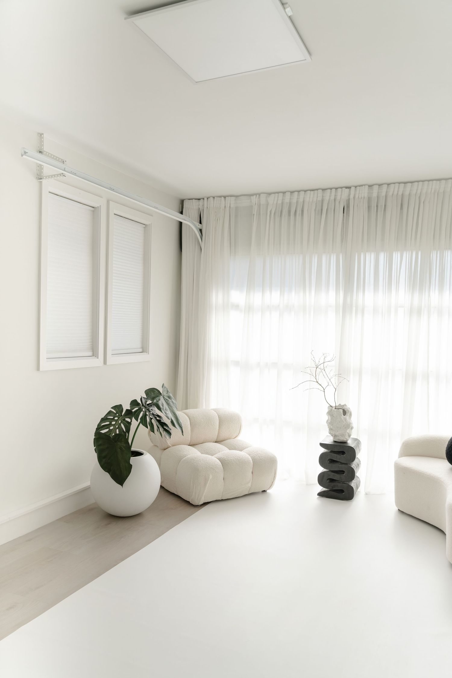 Bright white modern living space with curved sofa, decorative plants, and flowing curtains.