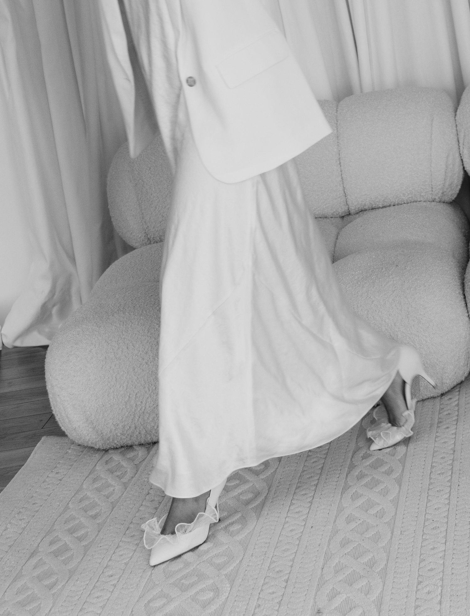Close-up of white flowing dress and silver shoes on patterned carpet.