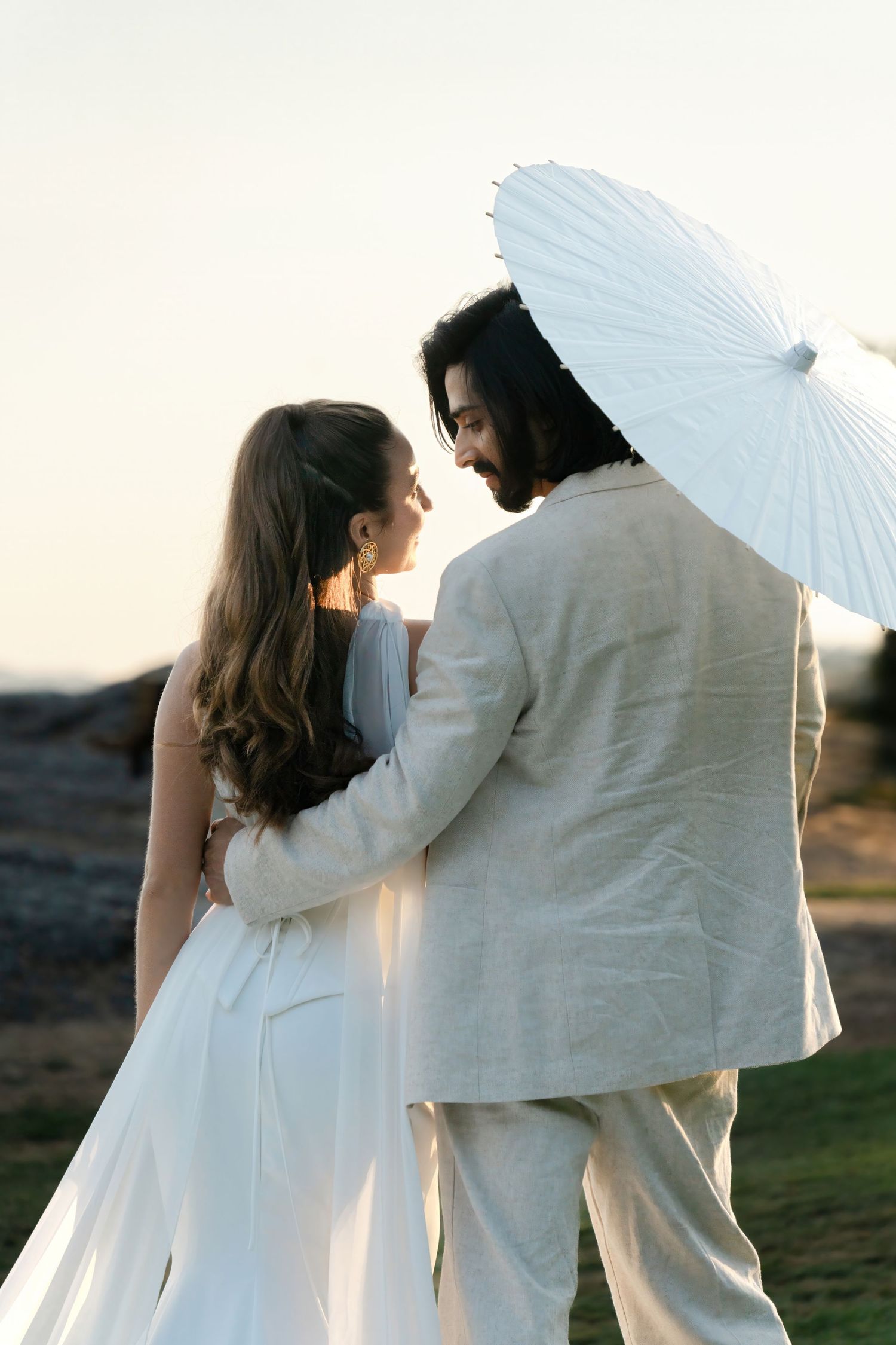 A romantic couple in white attire dance together with a white parasol creating an ethereal silhouette sequence.
