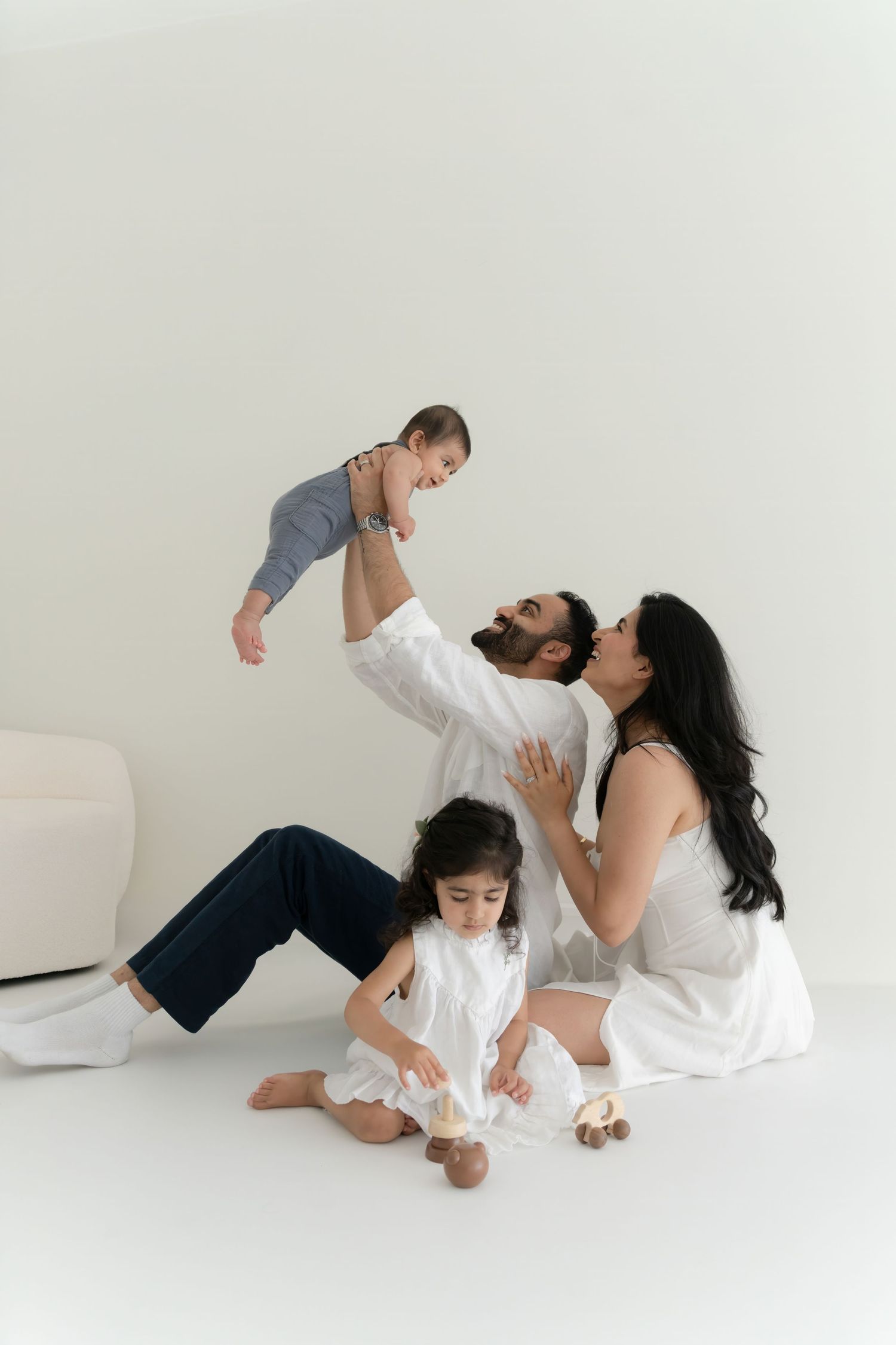 Family wearing white clothing plays and poses together on white floor in minimalist studio setting.