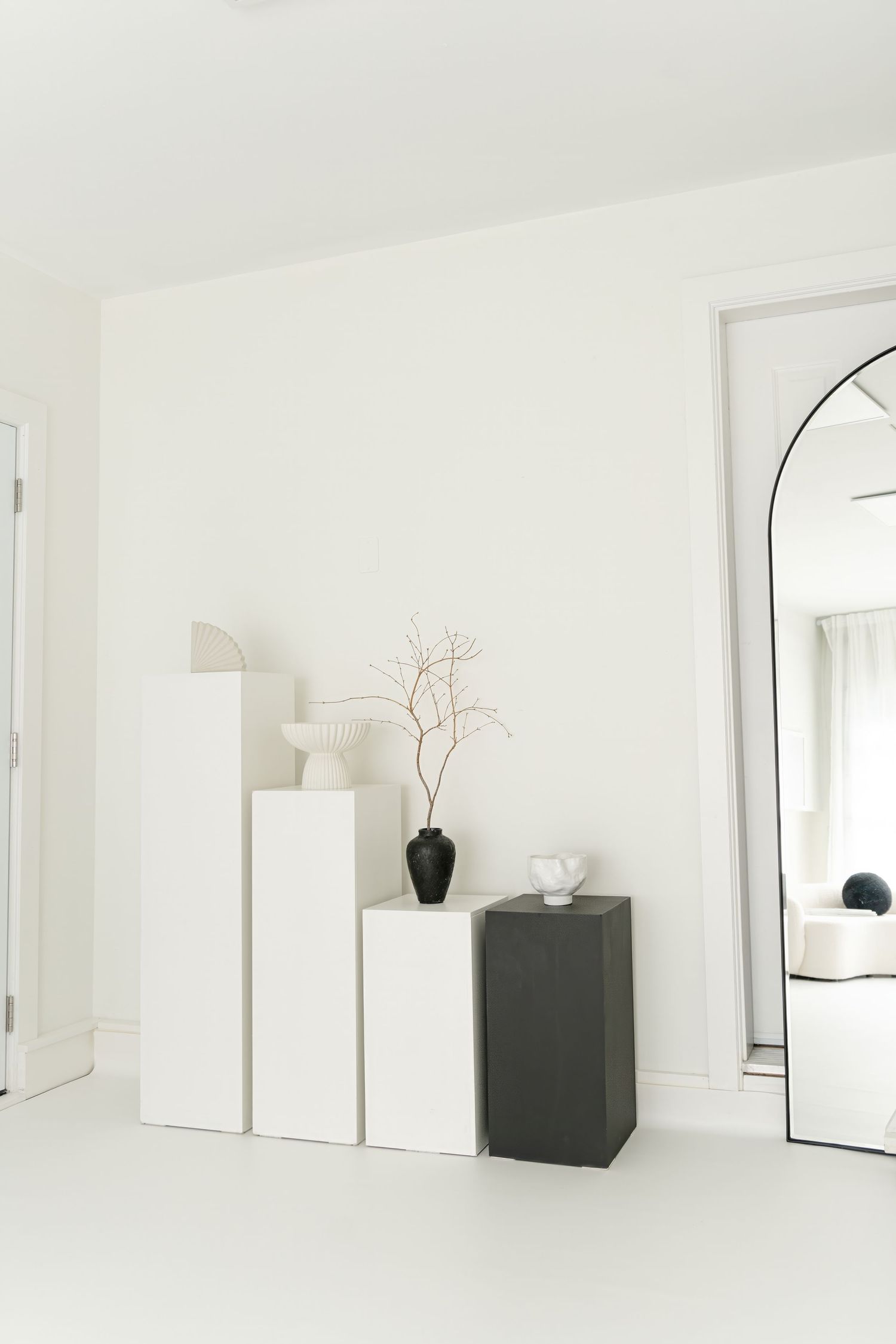 Minimalist white interior with stepped pedestals and arched mirror display.