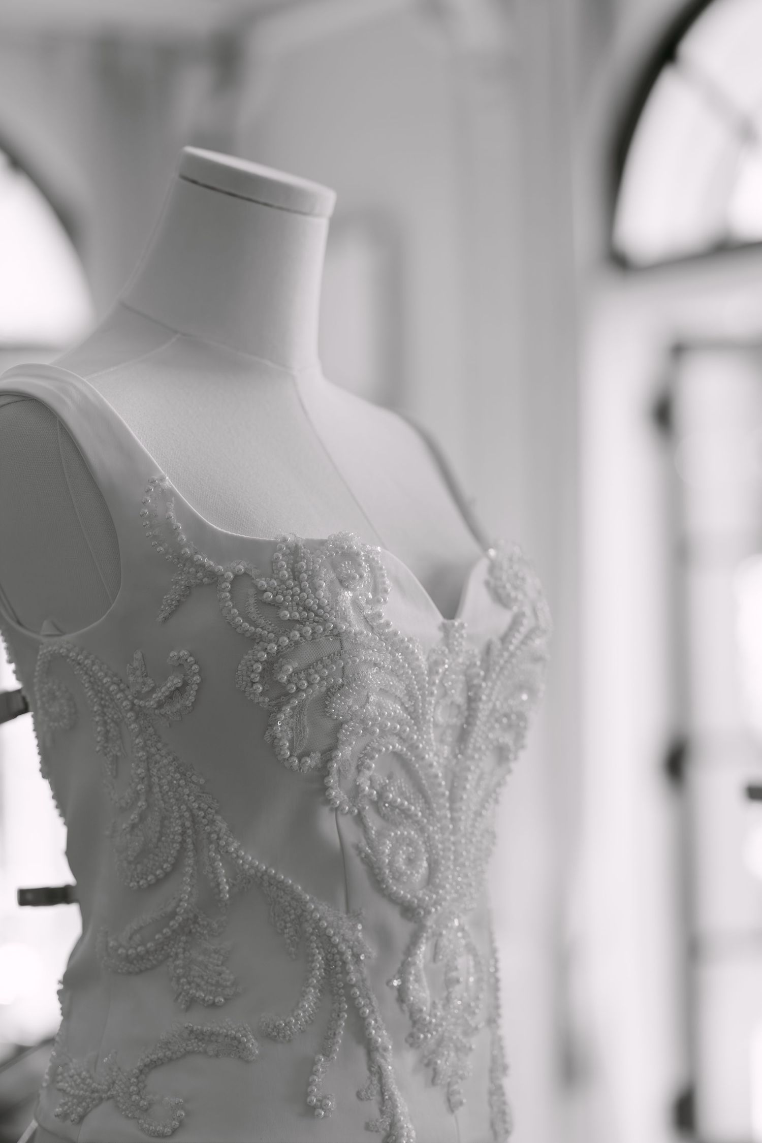 Elegant beaded lace wedding dress displayed on a mannequin in black and white photography.