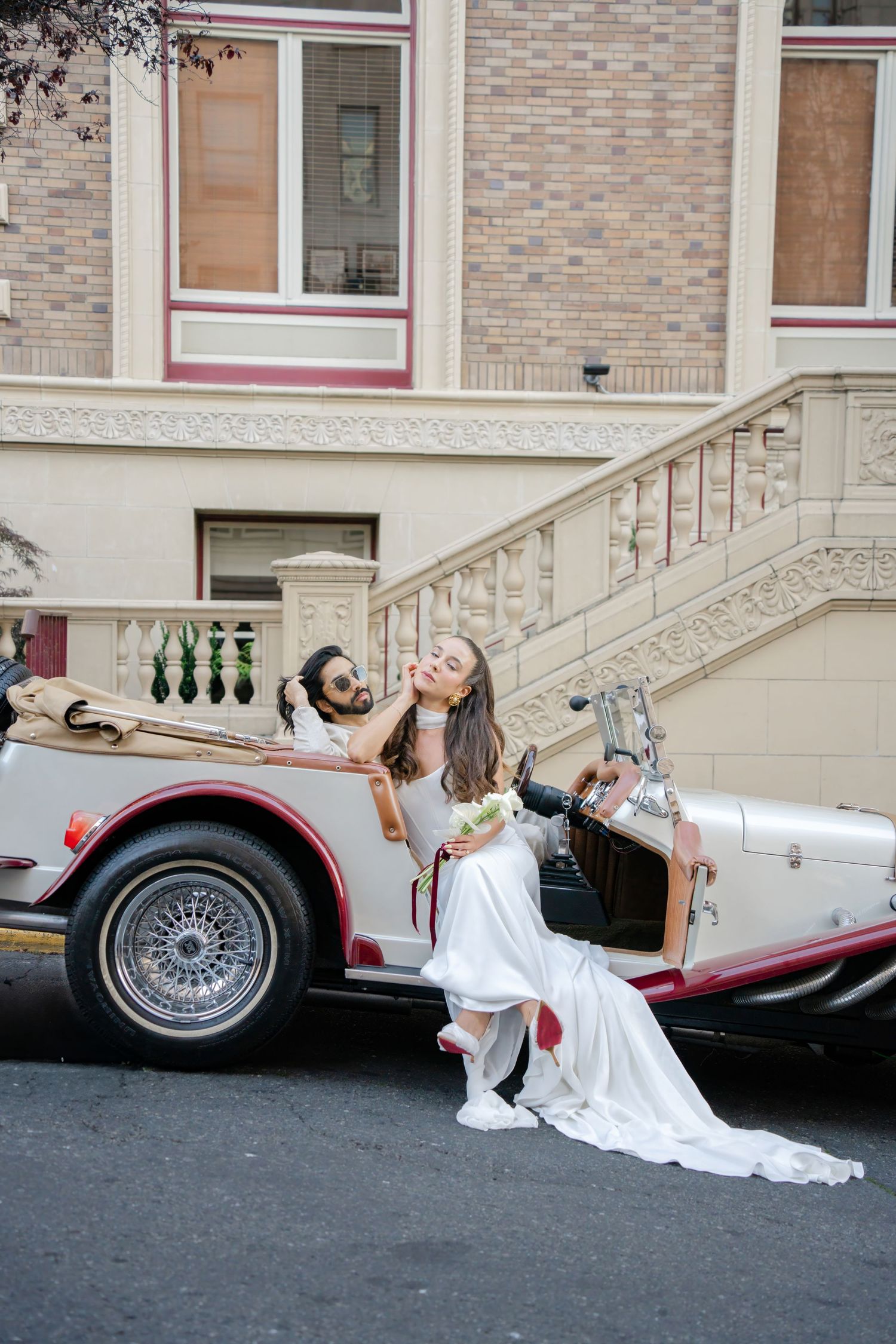 A vintage white and red classic car parked in front of a brick building with ornate stone staircase.