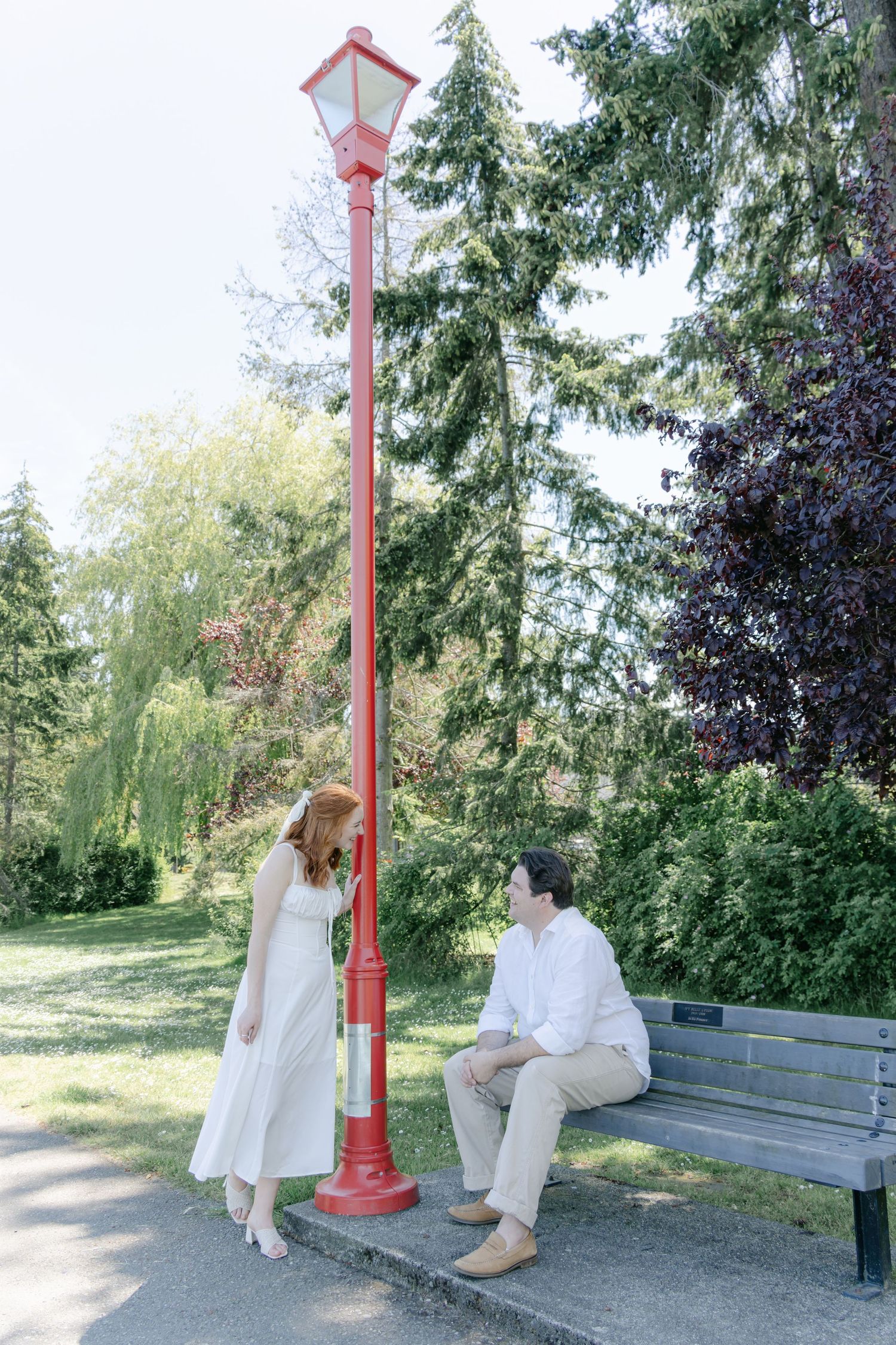 A sequence showing two people in white clothing sitting and interacting on a red-posted park bench.