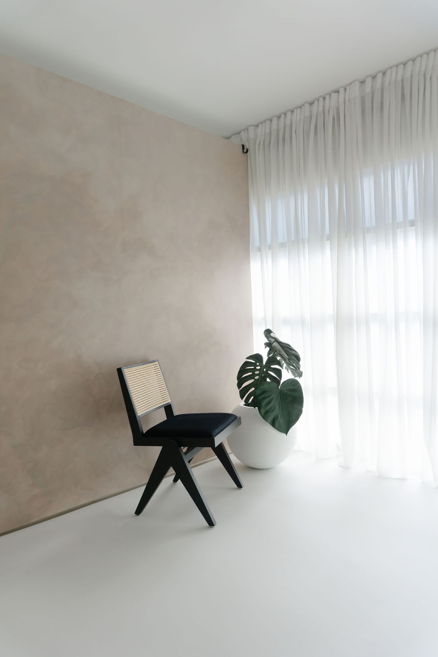 Modern black chair with monstera plant leaf in minimalist white room with natural window light.