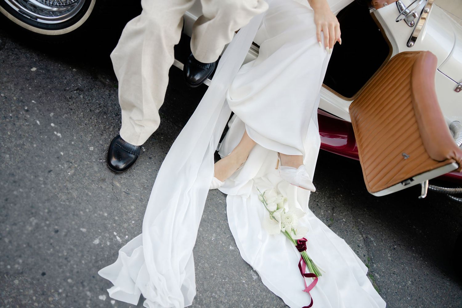 A bride in a flowing white wedding dress holds a bouquet while walking outdoors on a sunny day.