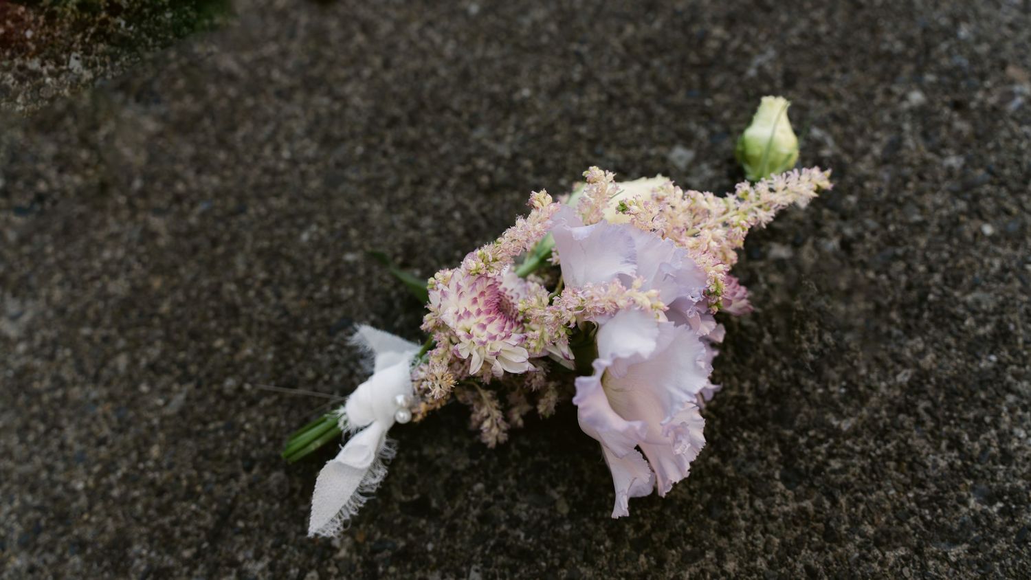 Delicate pink and white floral boutonniere lying on dark asphalt.