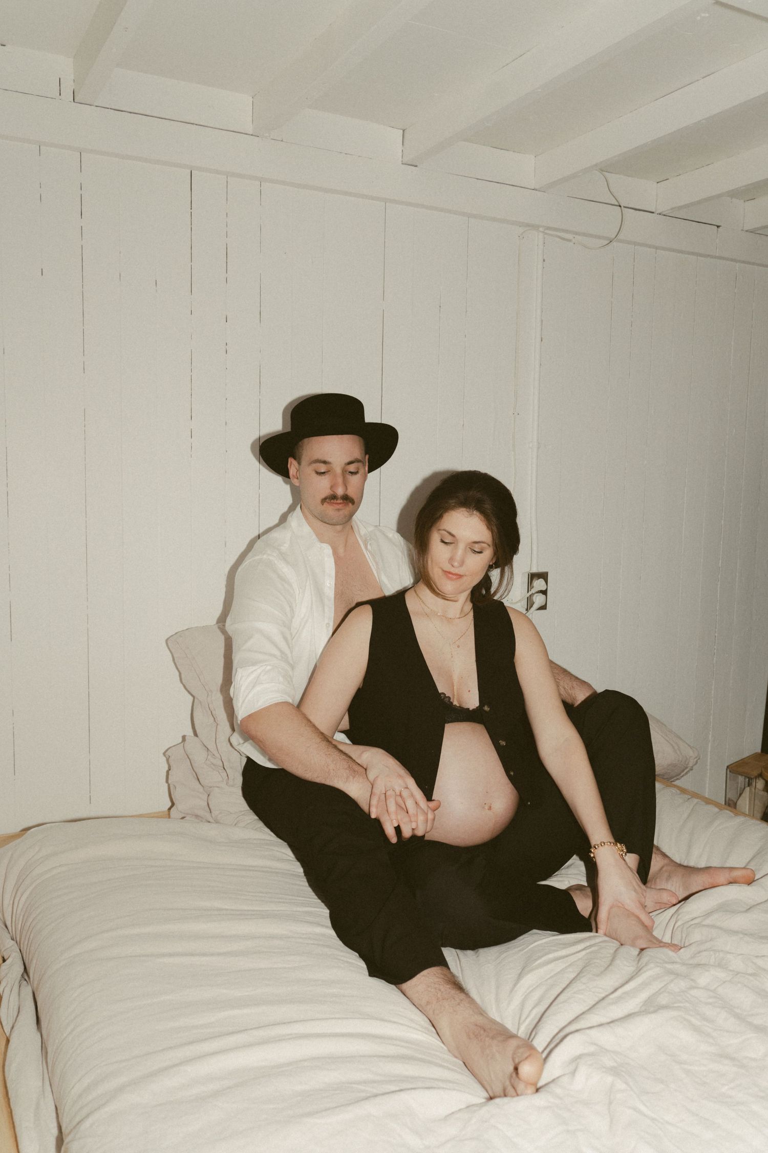 Intimate couple in vintage style clothing relaxing on white bedding in rustic room setting.