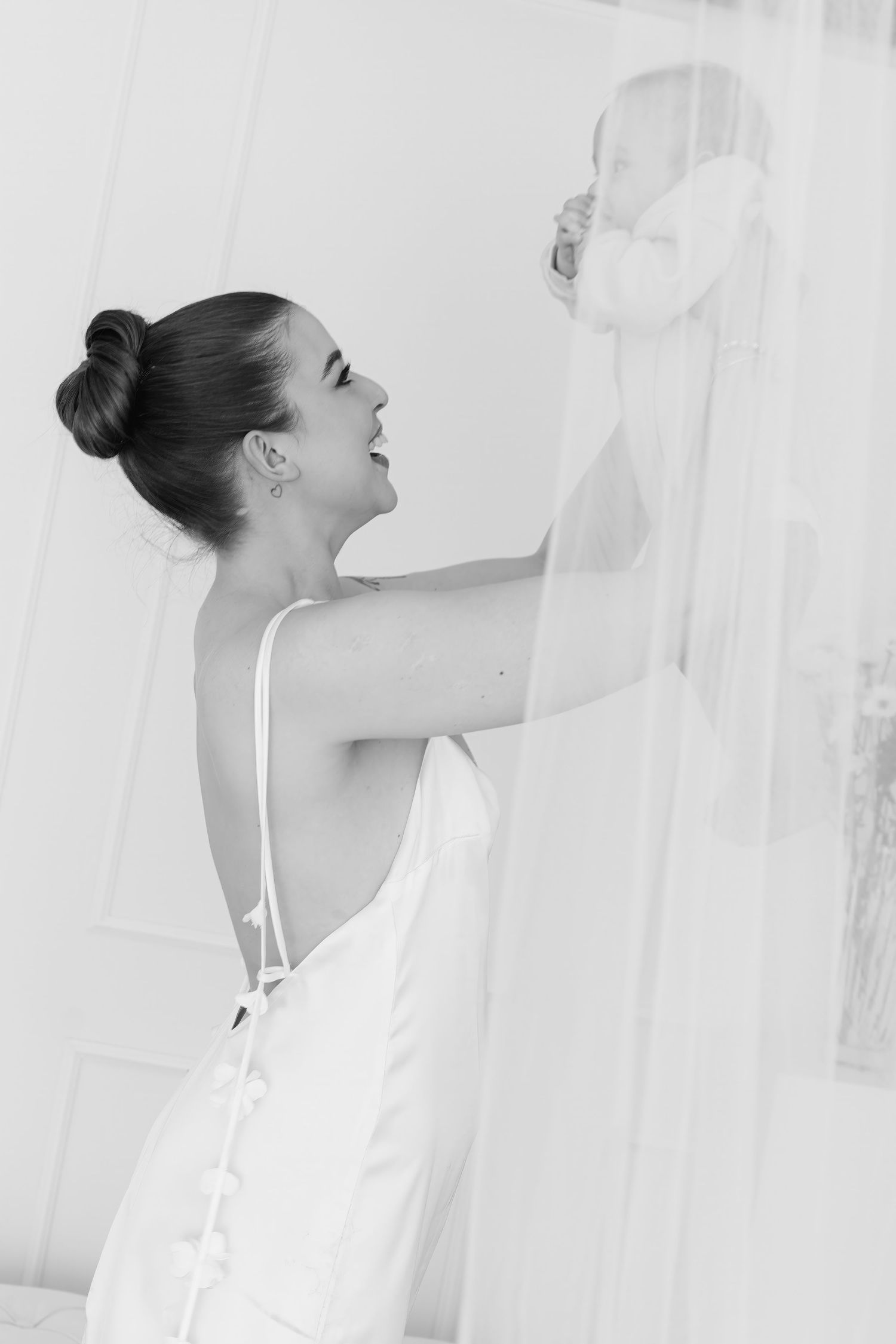 Profile view in black and white showing elegant posture against sheer curtains.