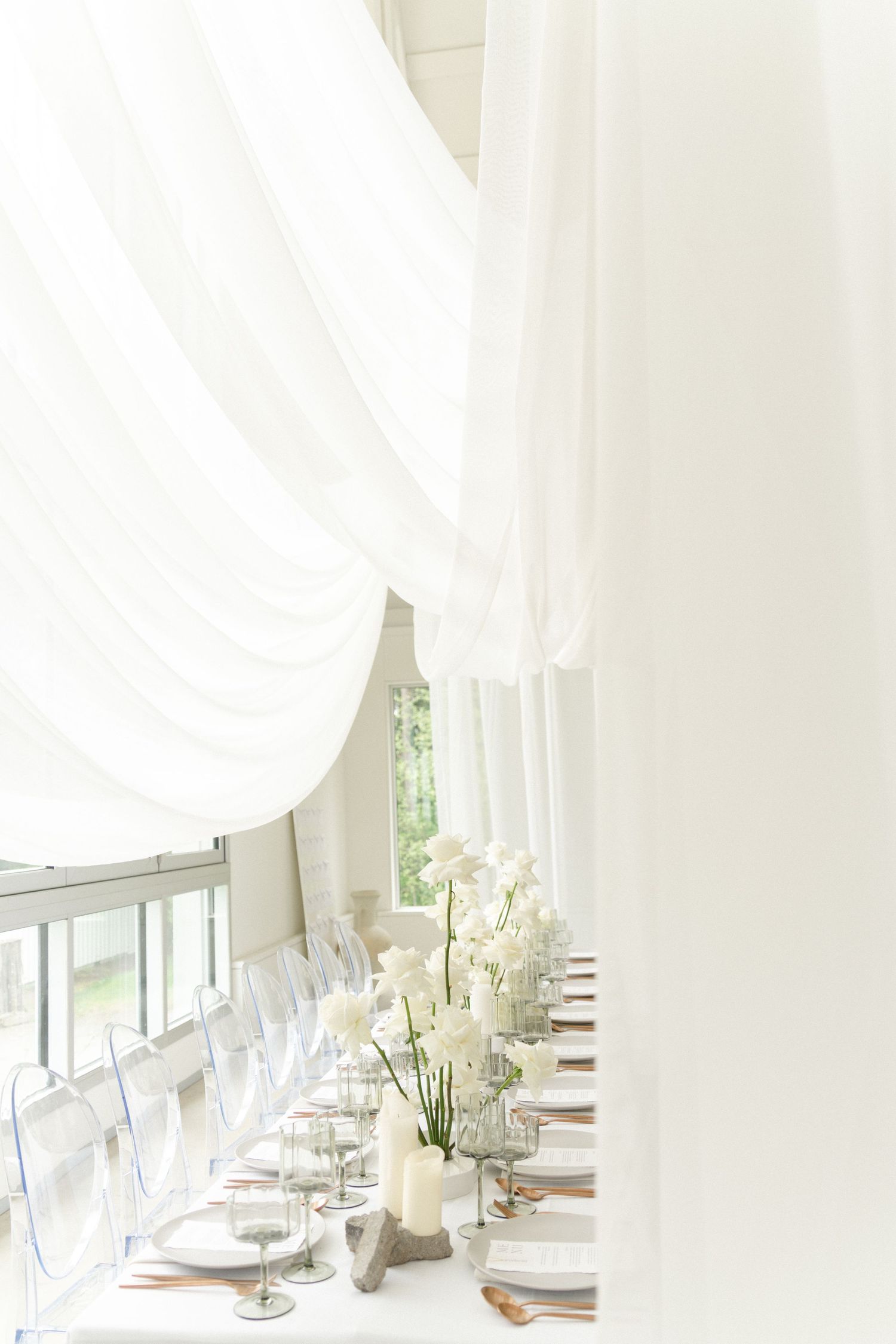 Elegant all-white wedding reception table with flowing curtains and natural light.