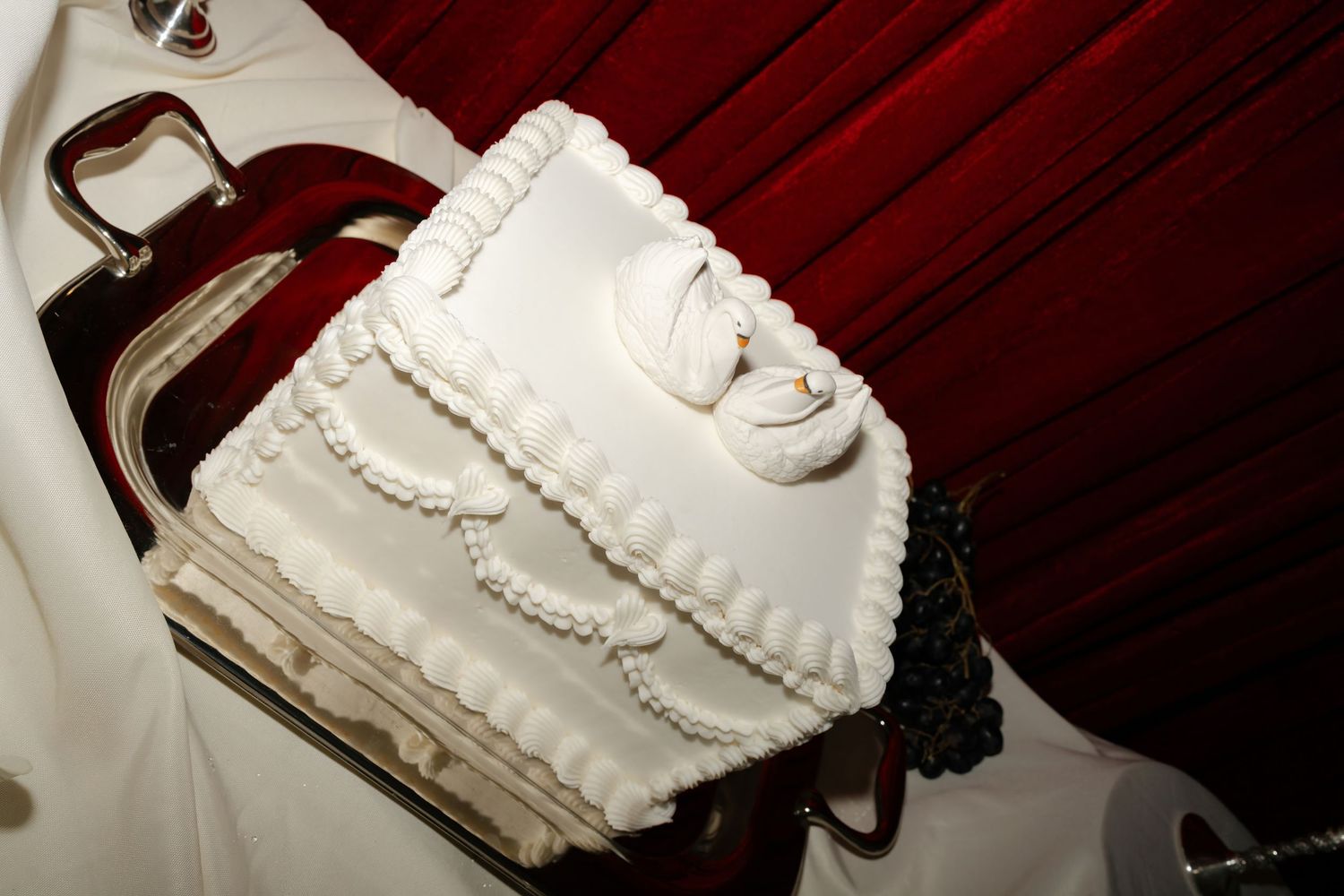 A white wedding cake being sliced with a silver knife on a dark wooden table.