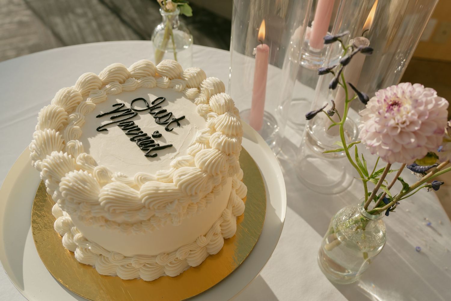 A white wedding cake decorated with delicate piping and a pink candle on top.