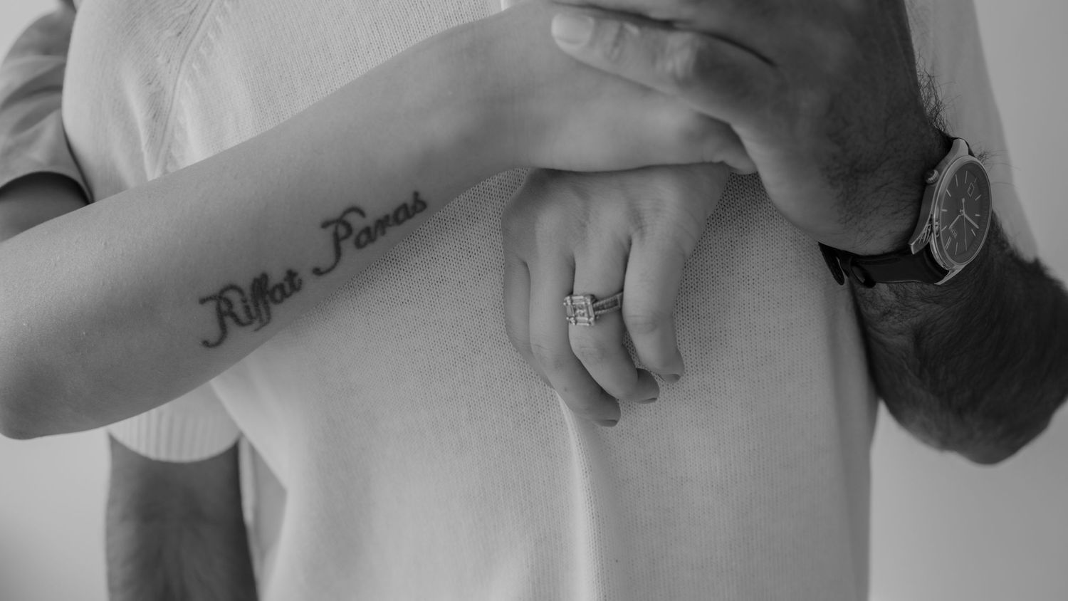 Close-up of hands showing tattoo and wedding ring against white background.