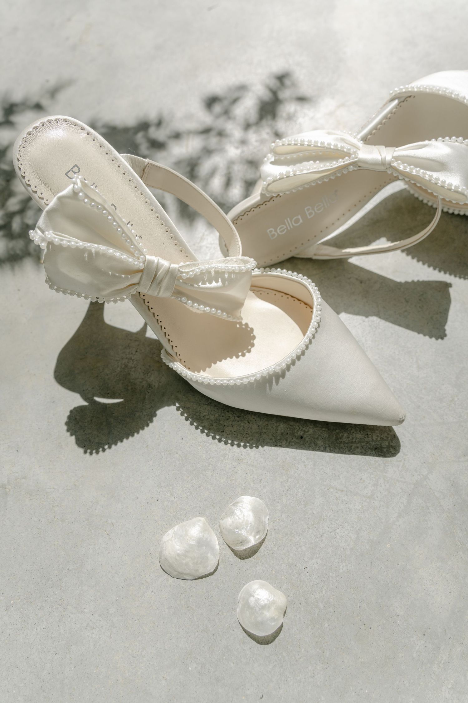 Delicate white bridal shoes with pearl details on a textured surface.