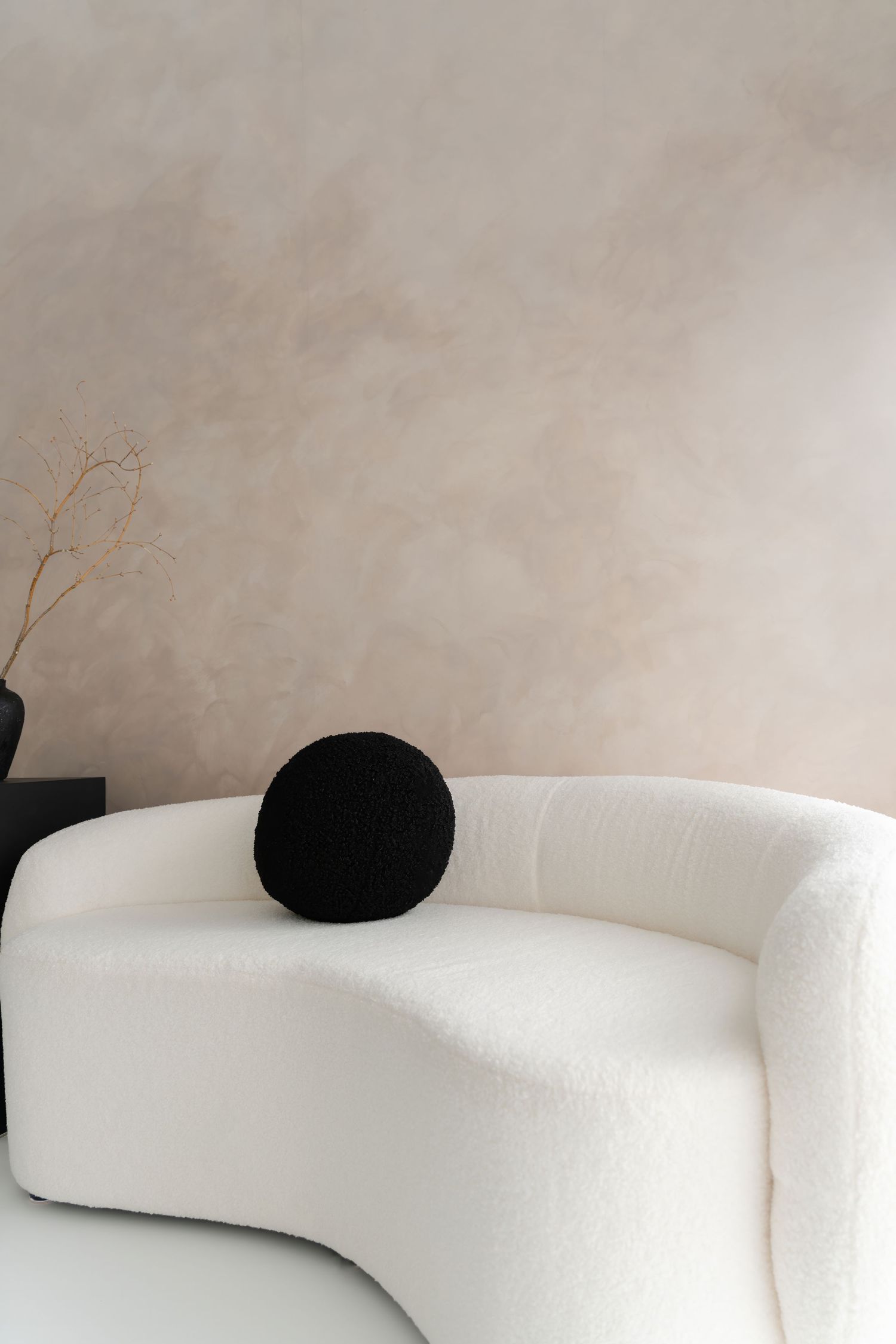 Minimalist curved white sofa with black round cushion against neutral wall.