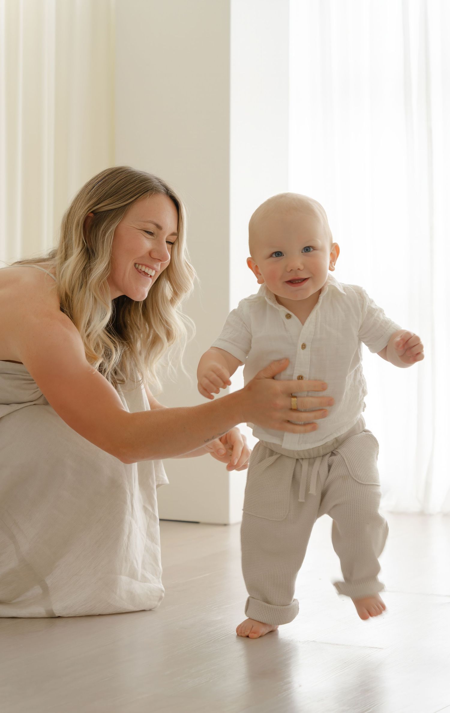 A heartwarming moment of supporting first steps in a bright white room.