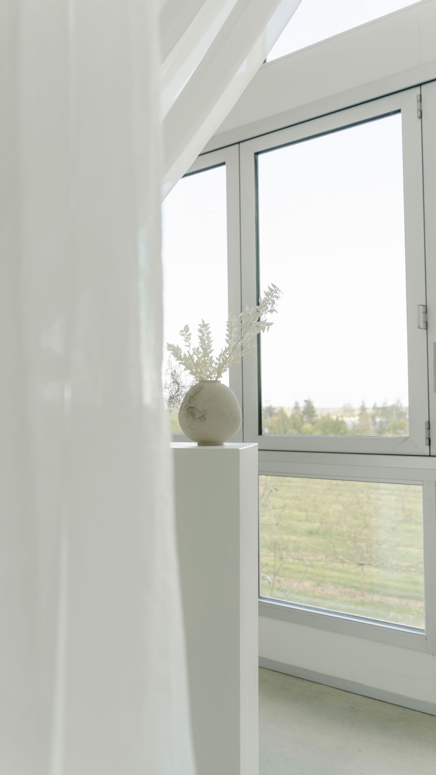 Modern white interior with curved archways and large windows overlooking a green landscape outside.