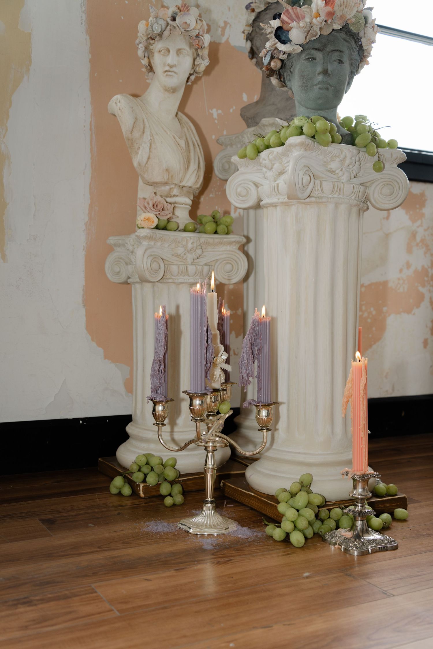 Classical busts and candles create an elegant tablescape with grapes and white columns on distressed peach walls.