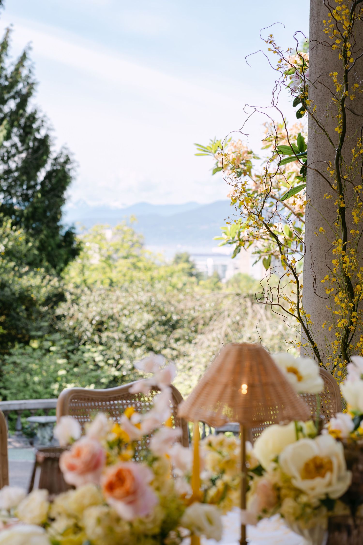 Romantic outdoor wedding tablescape with peach roses, yellow flowers, and rattan lamp with mountain view.