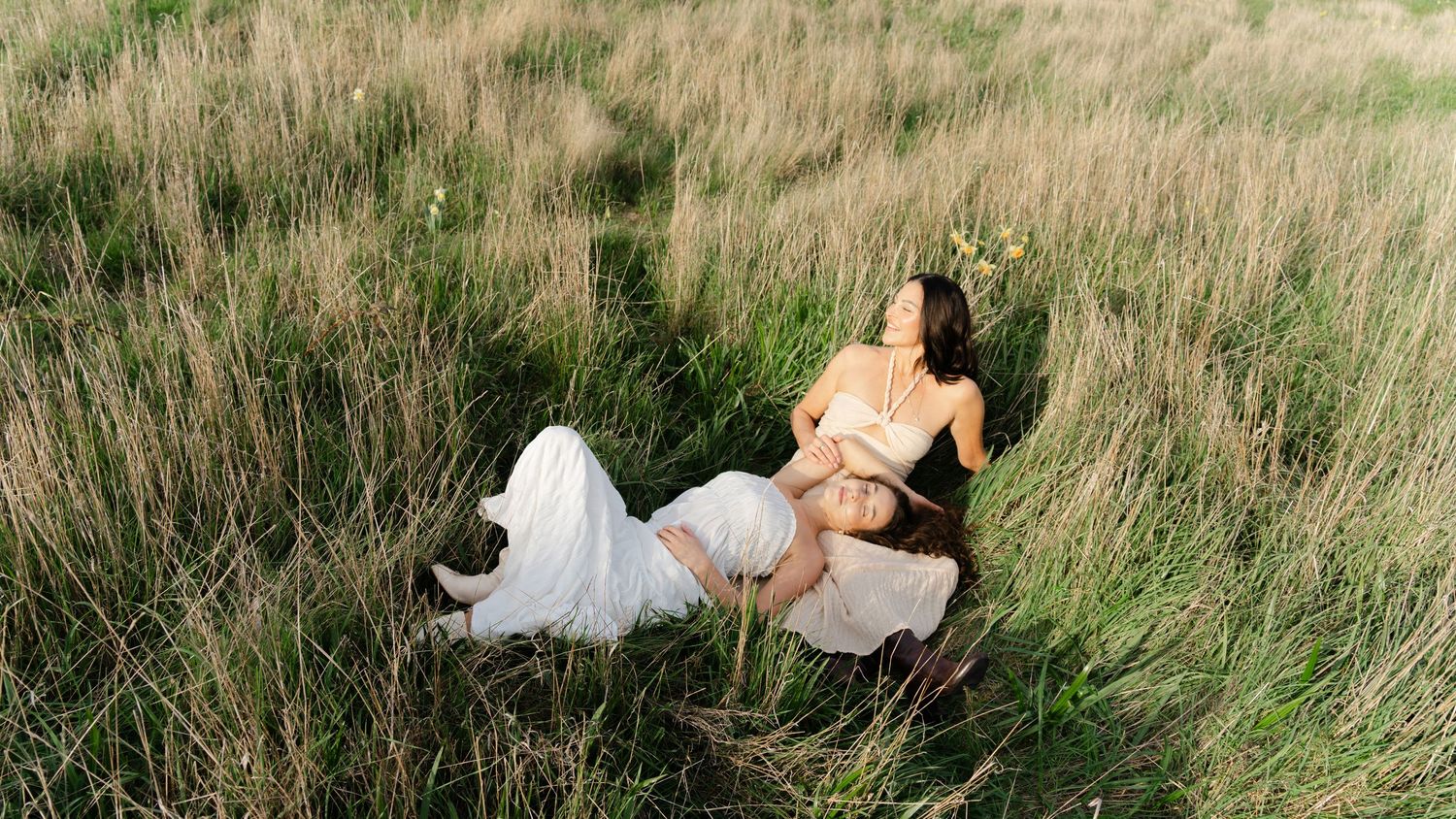 Two people relaxing in tall grass on a sunny day wearing white and light colored clothing at Beacon Hill Park. Dallas Road