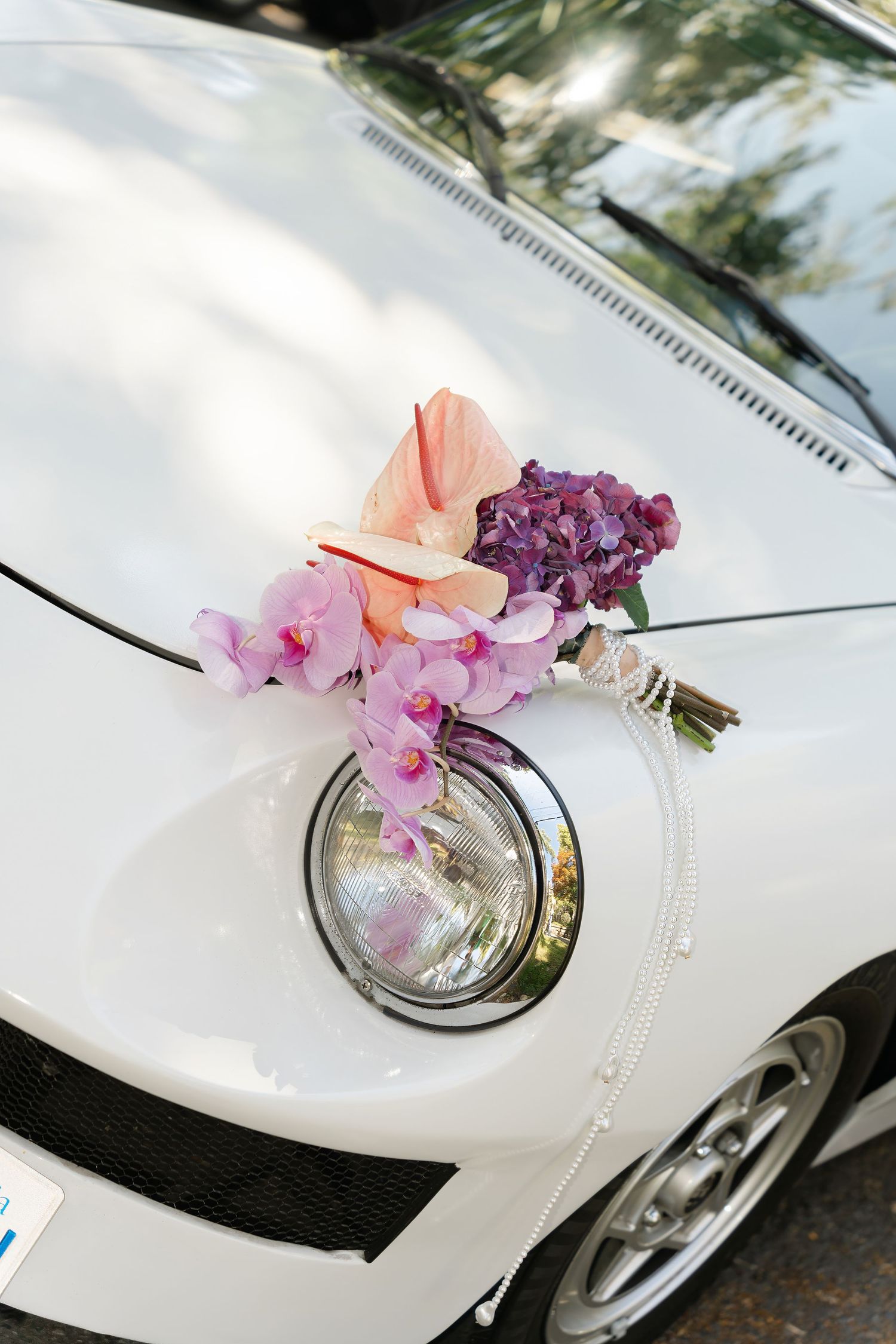 White car decorated with pink and purple flowers on the headlight for wedding.