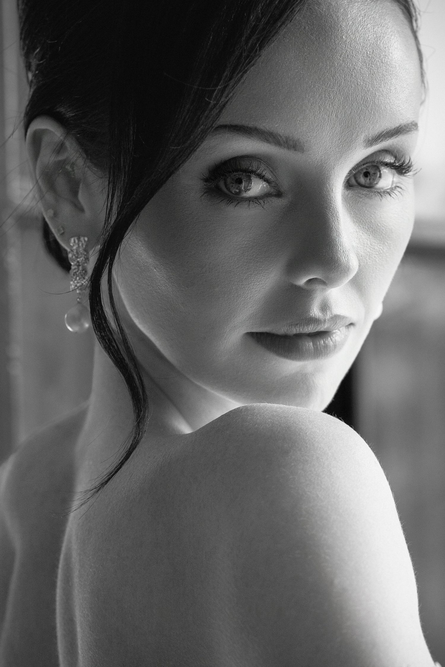 Black and white portrait of a young woman with dark hair, elegant earring, bare shoulder, and striking eyes.