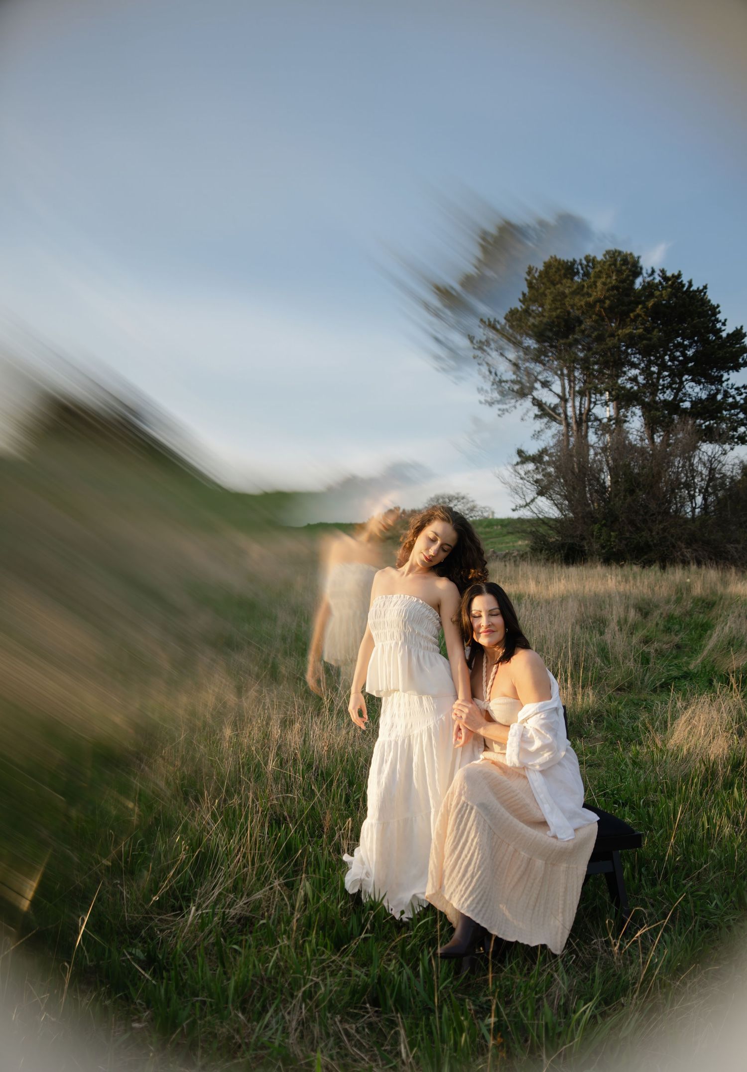 Artistic portrait of two people in flowing white dresses standing in a golden meadow.