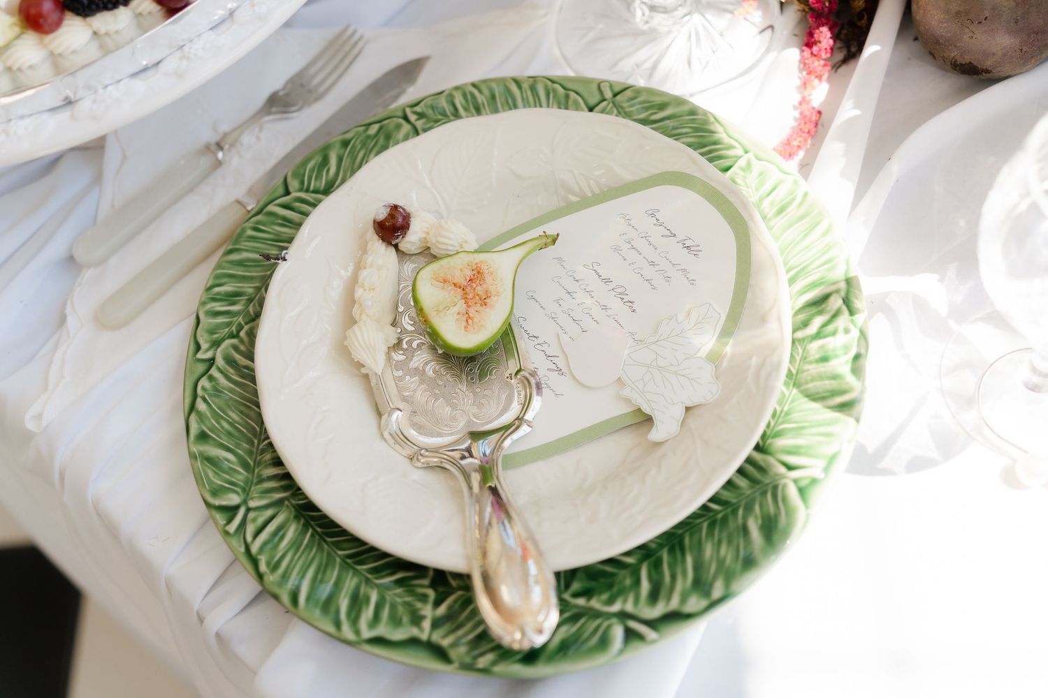 Table place setting with ornate green cabbage leaf charger plate and vintage silverware.