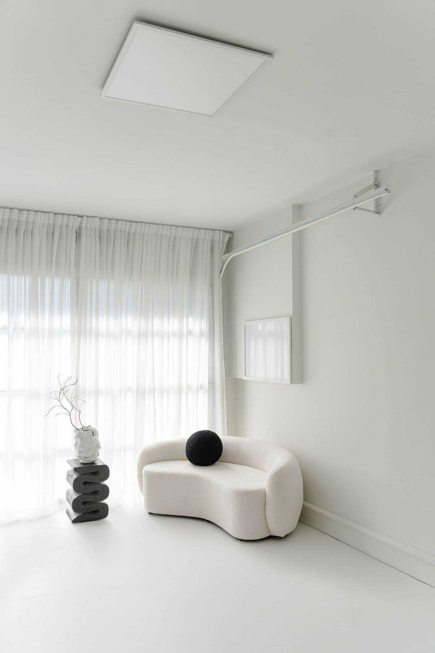 Contemporary white room with curved sofa and stacked stone sculpture near sheer curtains.