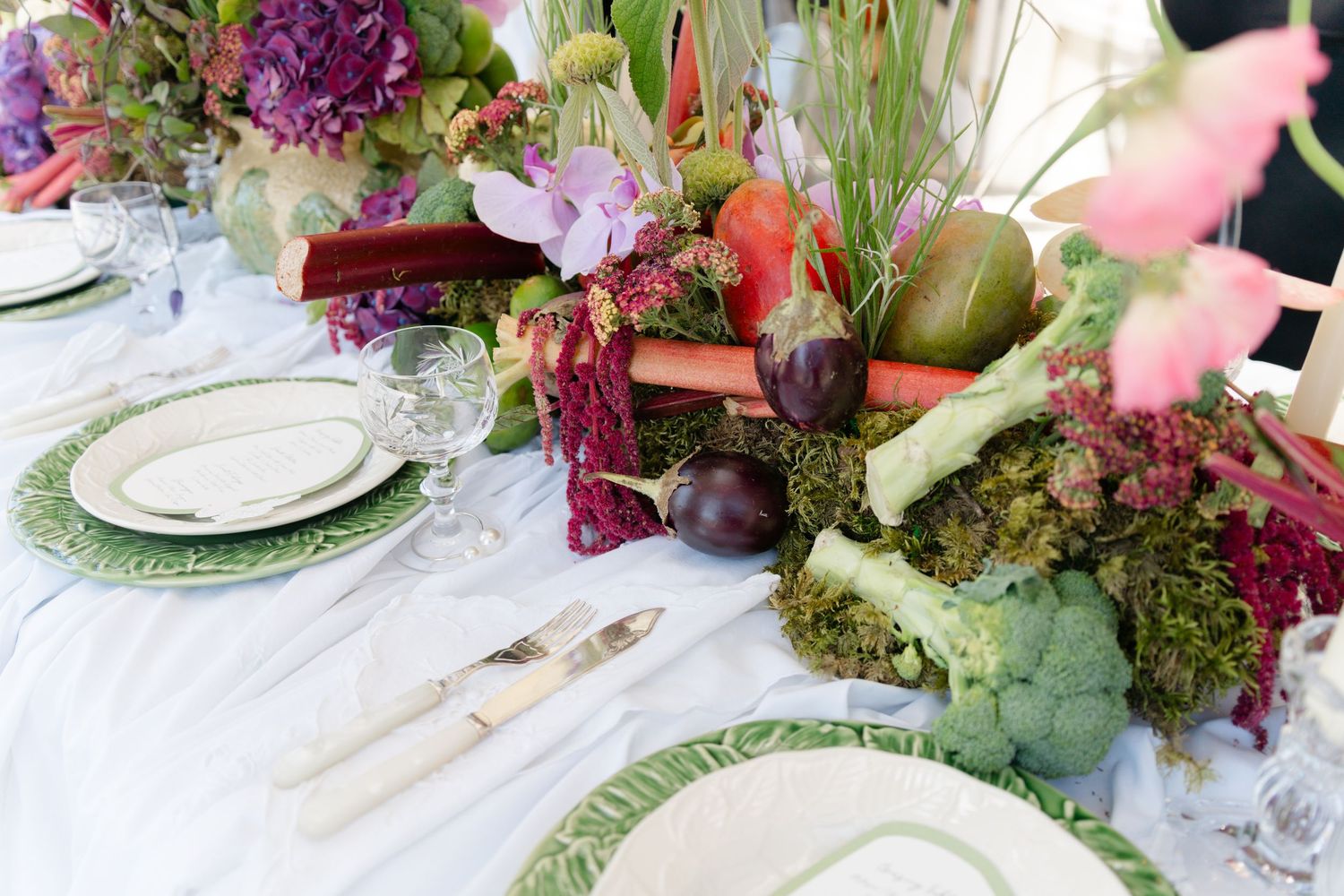 Elegant table setting with vibrant purple and pink floral arrangements and fine china on white tablecloth.
