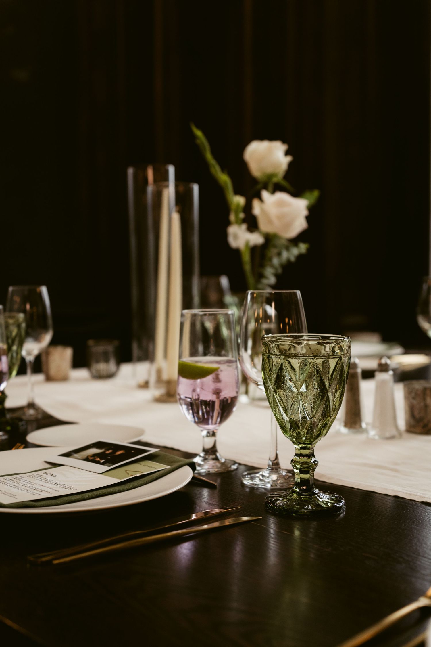 Elegant tablescape with crystal glasses, white candles and place settings for wedding reception.