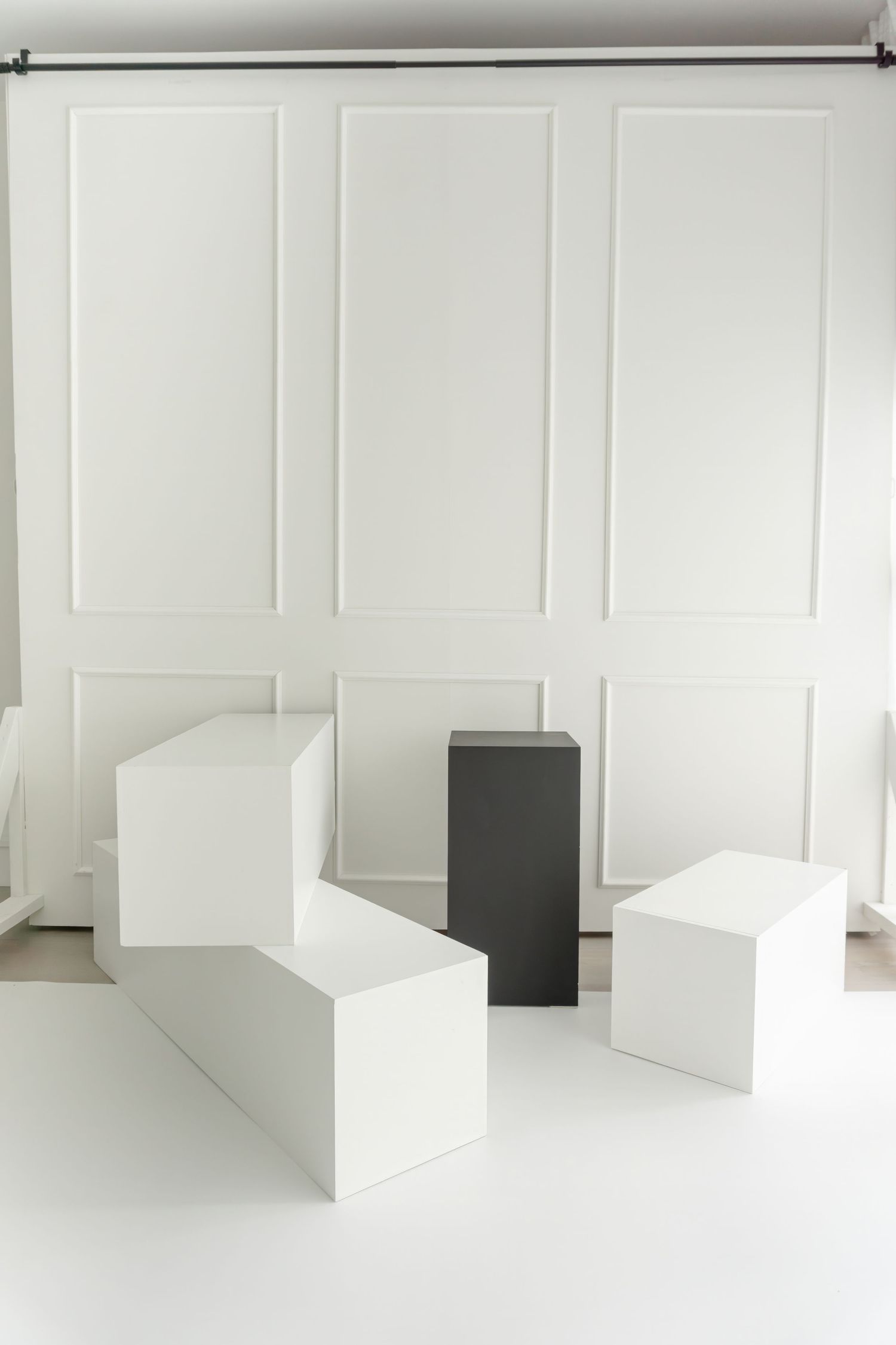 Clean white geometric blocks arranged in studio space with paneled walls and dramatic lighting.