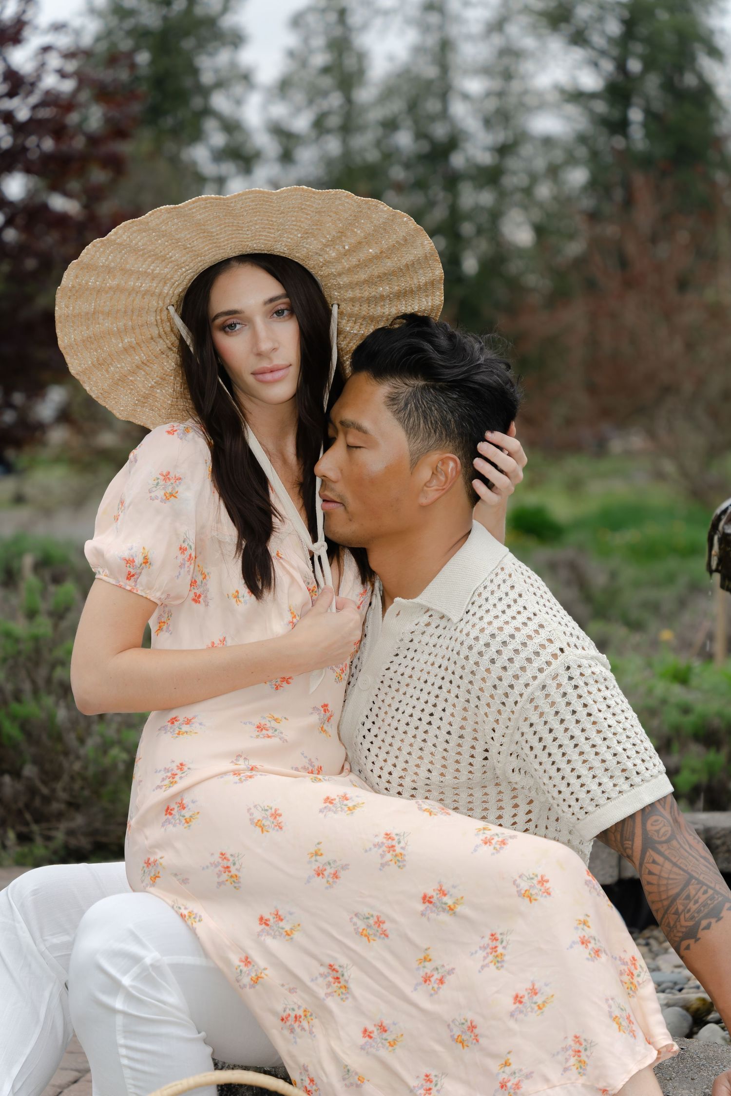 Couple in romantic poses wearing floral dress and white outfit with straw sun hats.