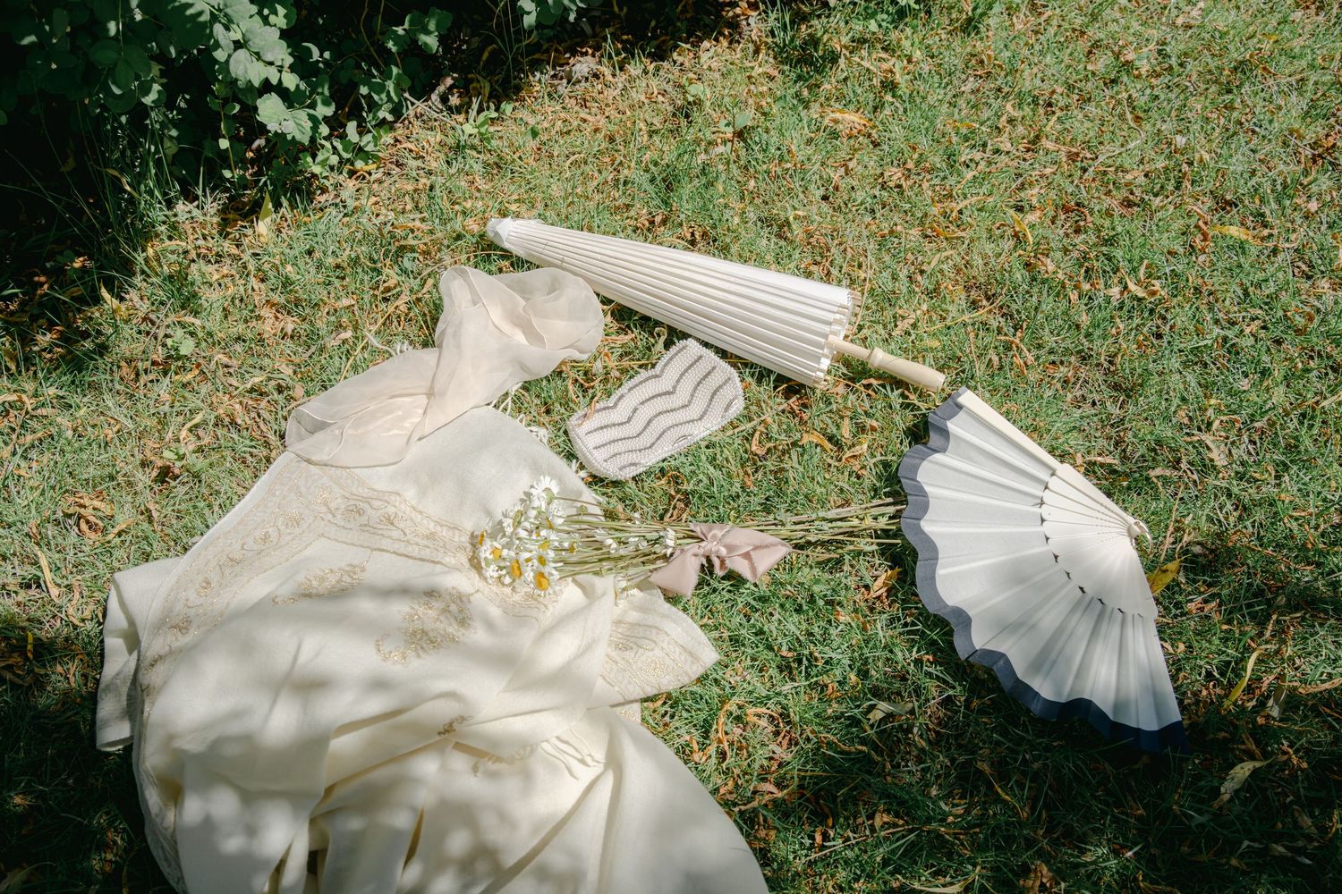 The hem of a white dress flows across green grass in a romantic garden setting.