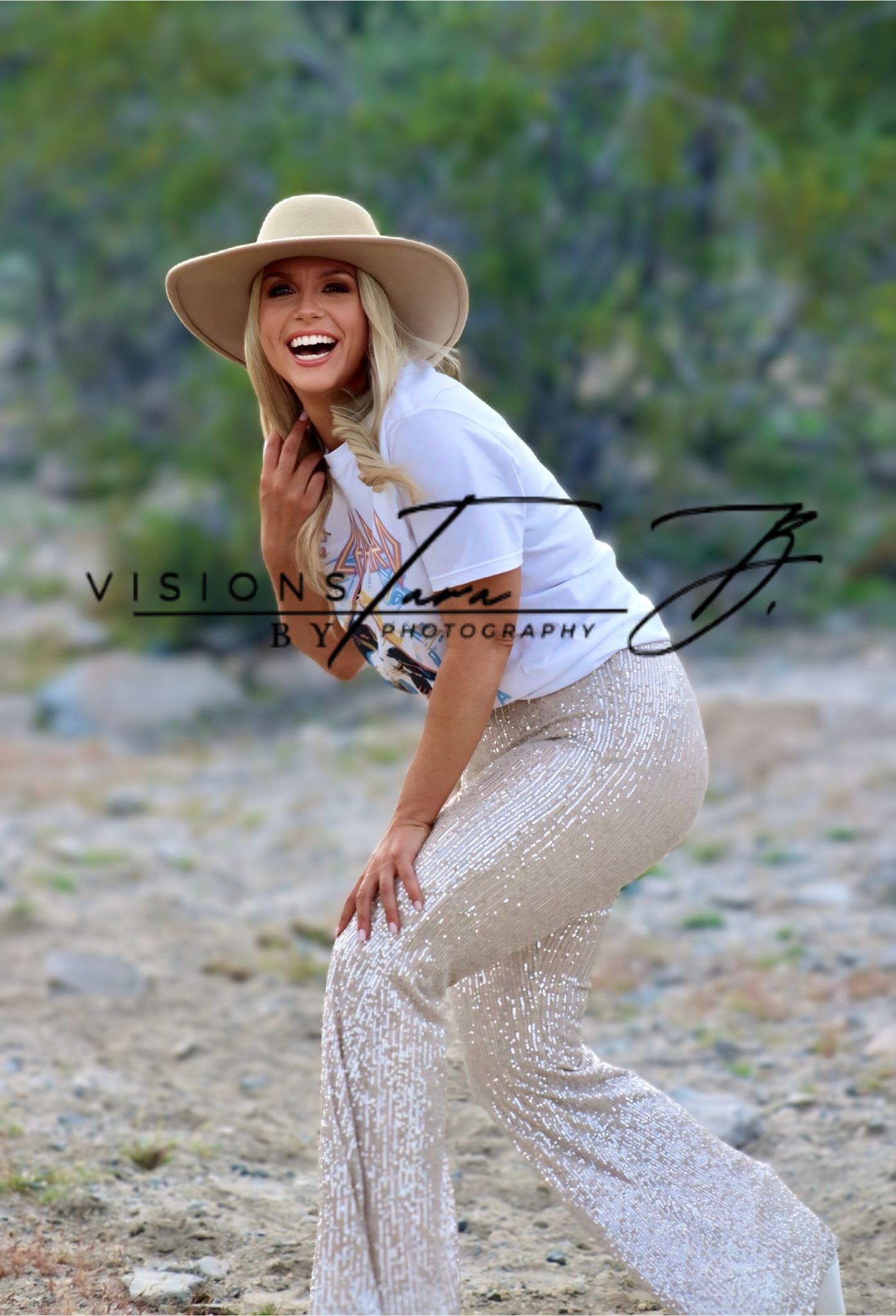 Woman laughing joyfully in the desert, wearing a hat and flowing outfit while moving through soft natural scenery.