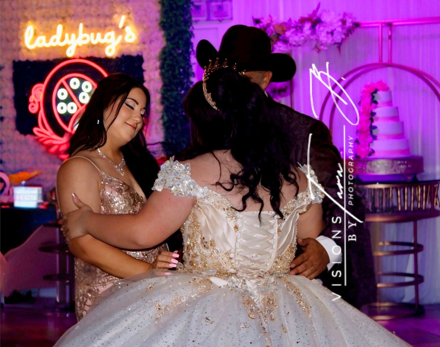Quinceañera in a sparkling gown hugging family members on a colorful dance floor during a joyful celebration.