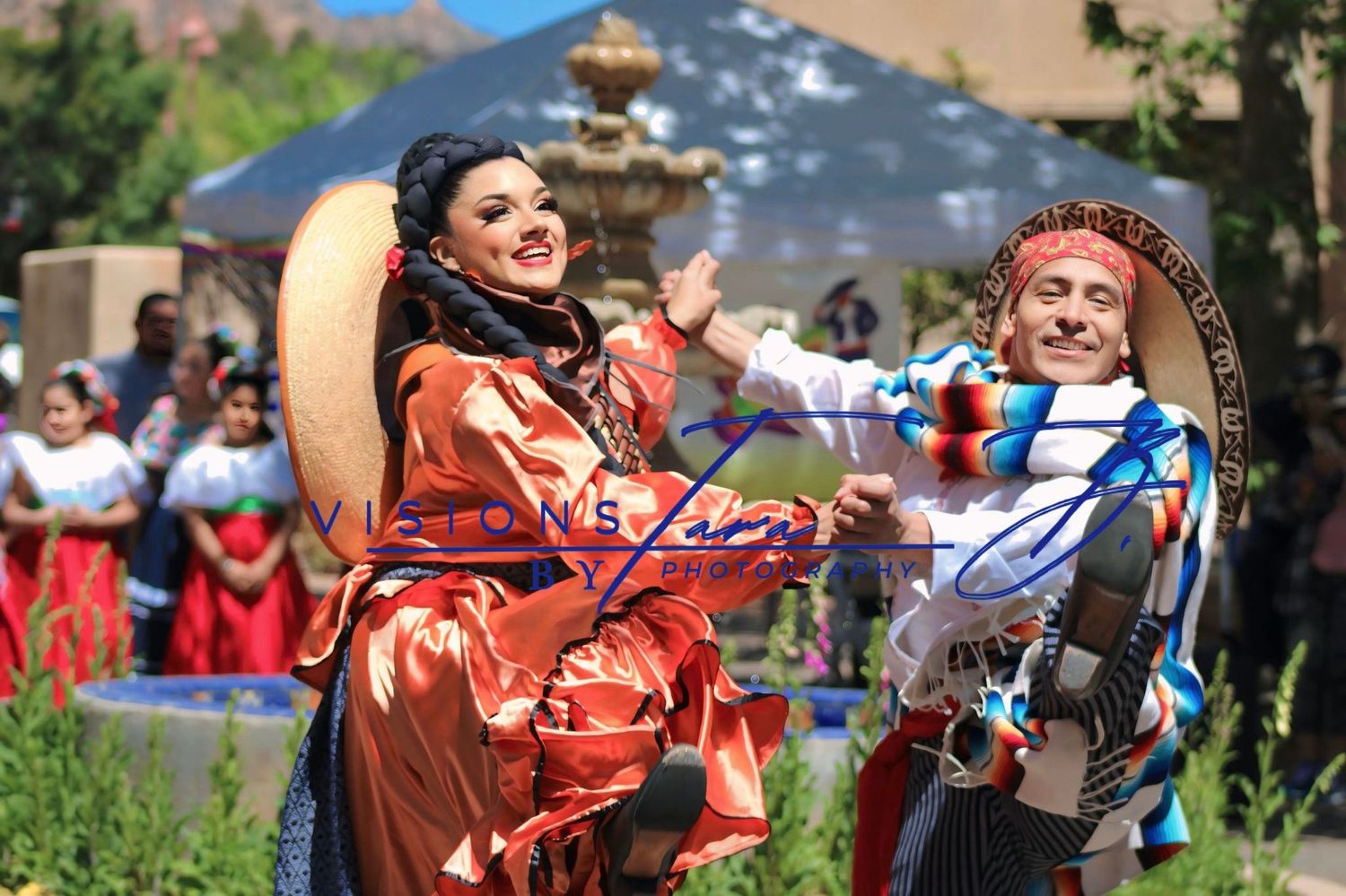 Two dancers in colorful traditional attire performing joyfully during a lively cultural celebration outdoors.