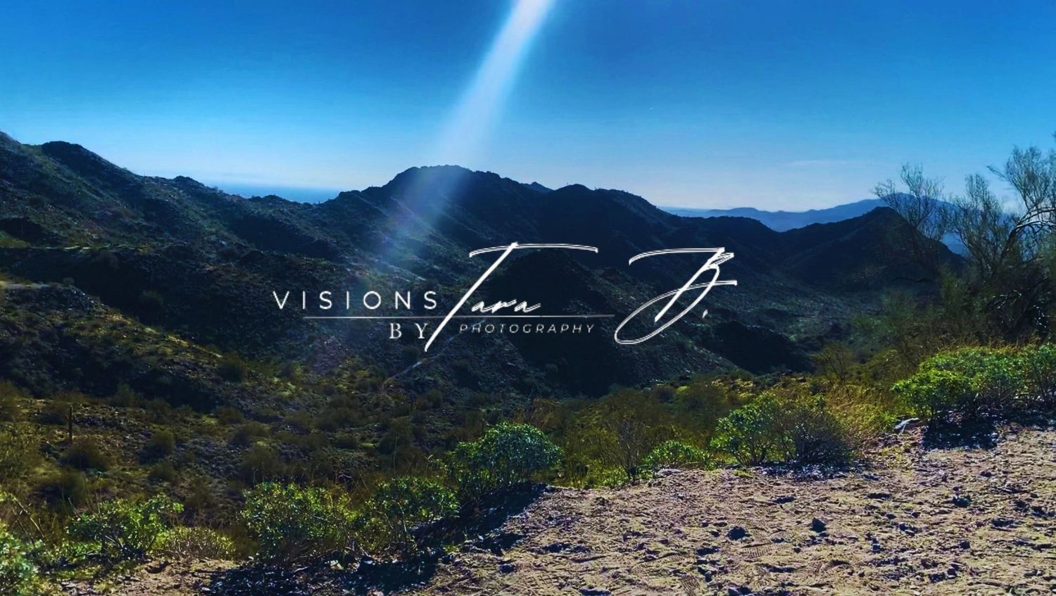 Sunbeam shining over rolling desert hills and blue mountains, creating a peaceful landscape under a bright sky.