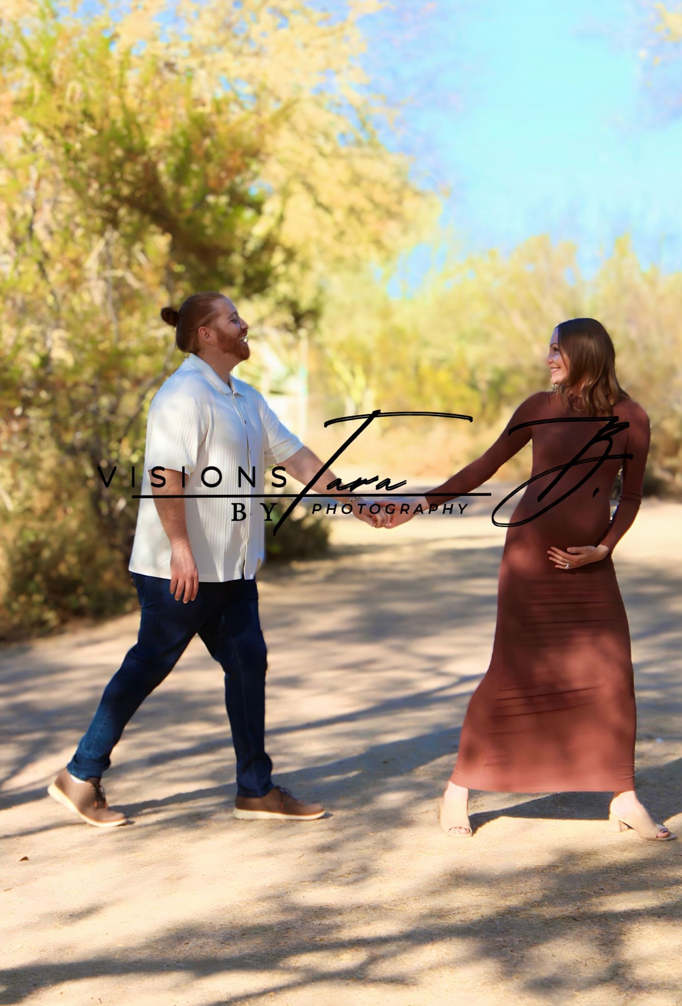 Pregnant couple walking hand in hand along a sunny path, smiling and enjoying a peaceful outdoor maternity moment.