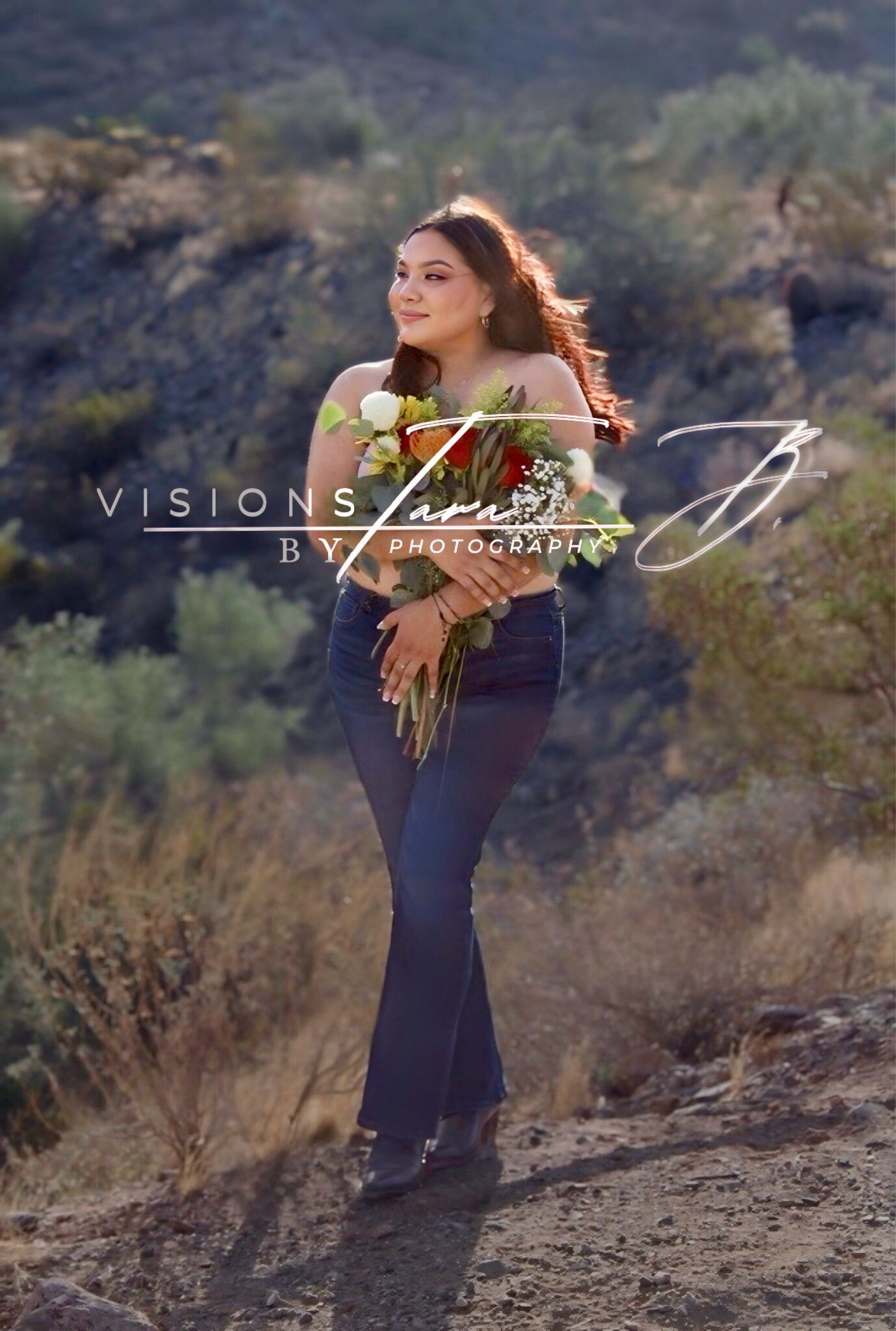 Woman holding a bouquet and standing in the desert breeze, captured in a soft, windswept portrait with natural scenery behind her.