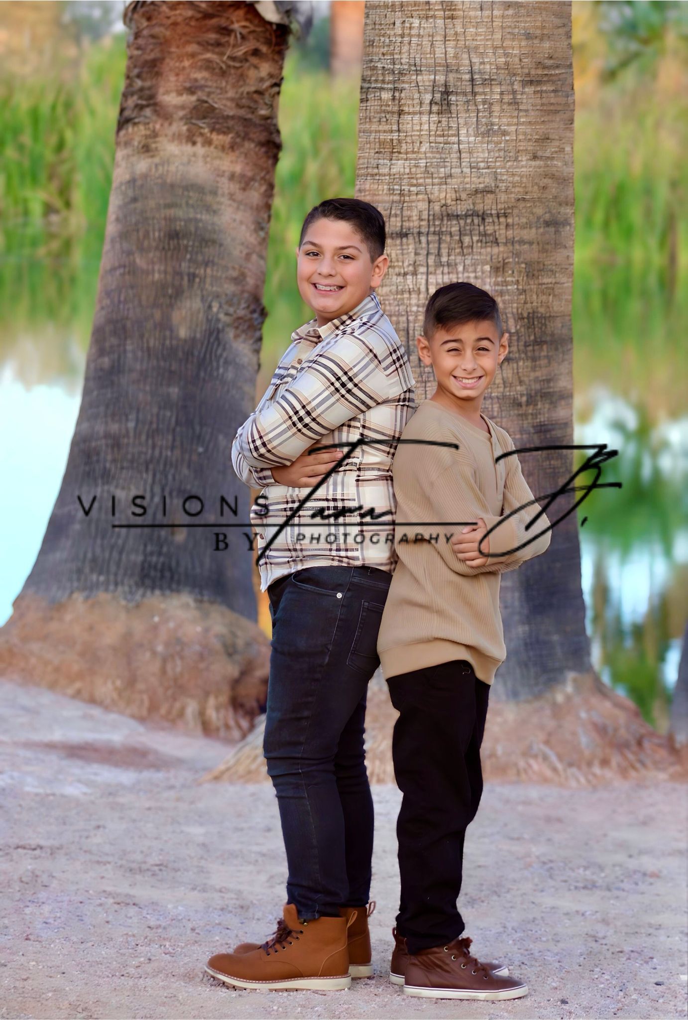 Two brothers standing back-to-back outdoors, smiling softly as they pose near a tree in natural light.
