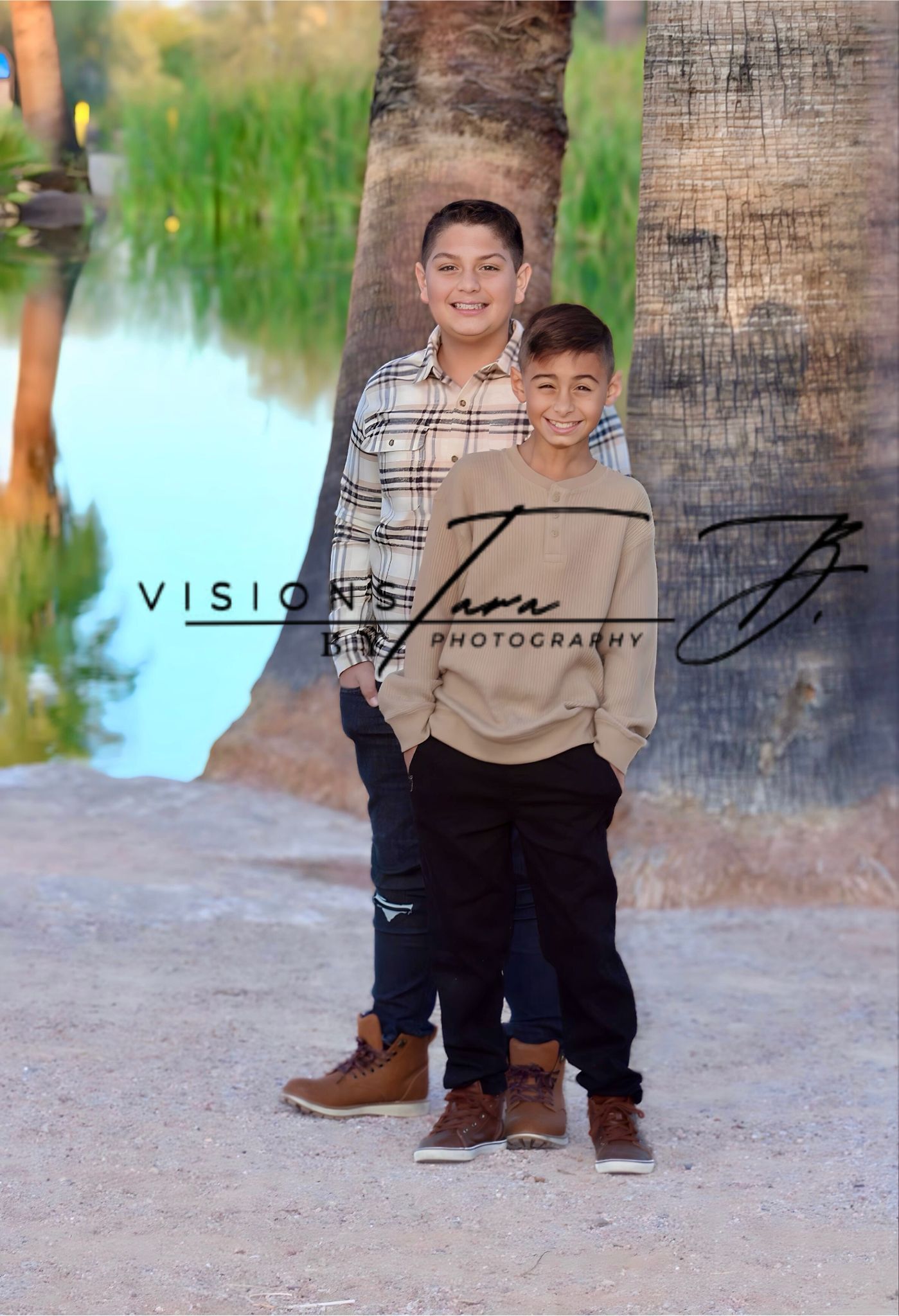 Young boy standing confidently by the lake, smiling as he poses for a portrait with water and greenery behind him.