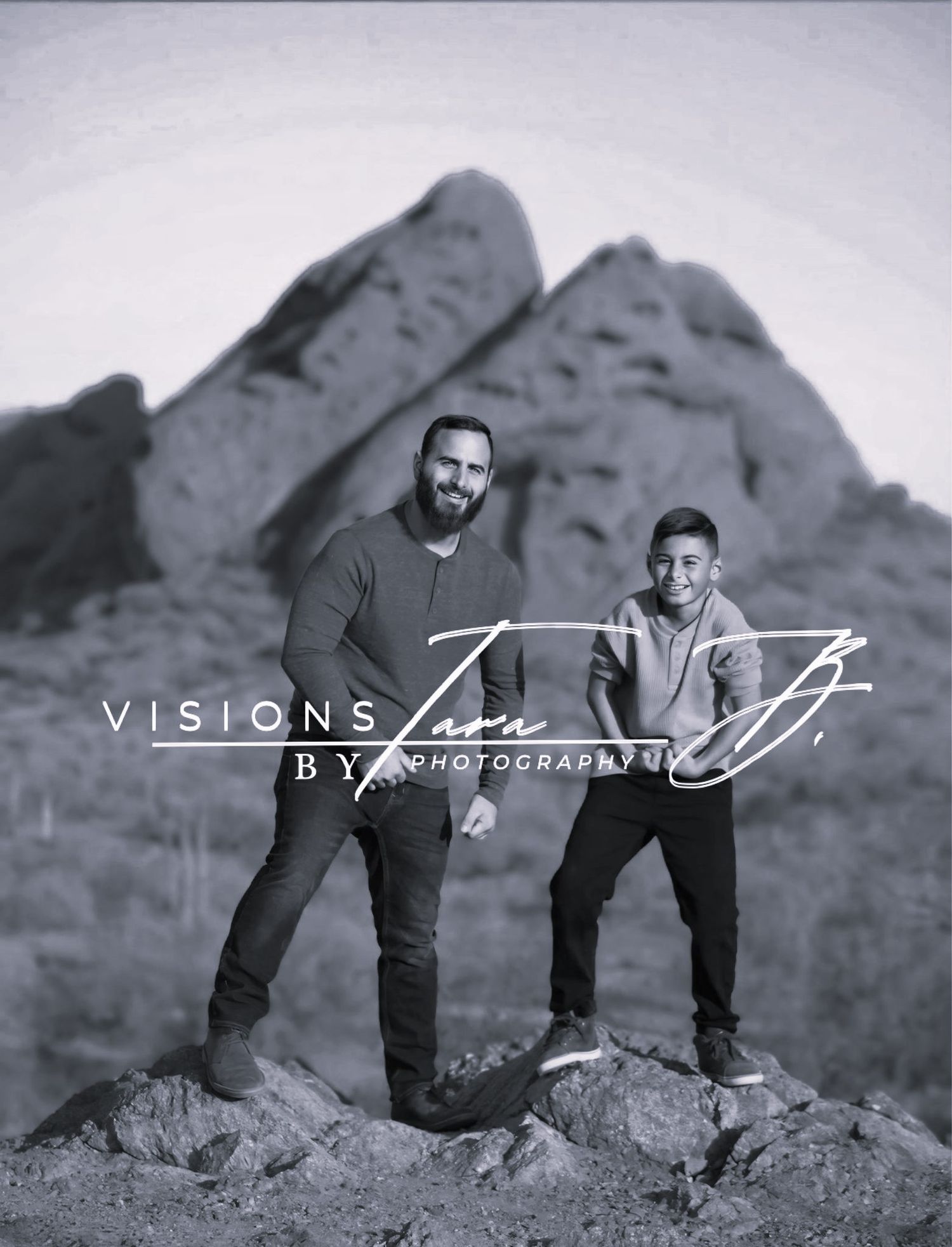 Black-and-white photo of a father and son holding hands while walking in the desert with mountains rising behind them.