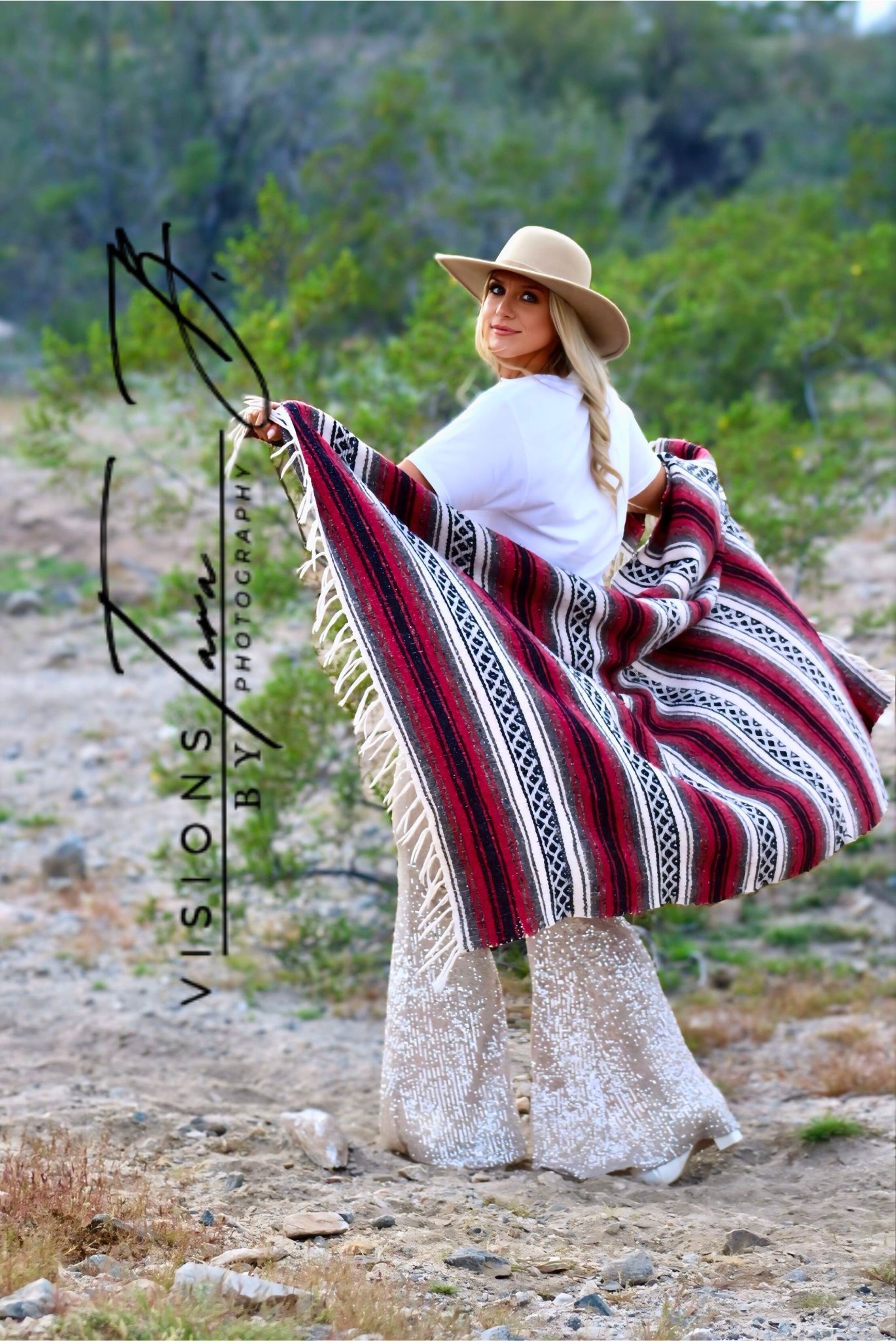 Woman walking through the desert wrapped in a patterned blanket, glancing back with soft natural light around her.