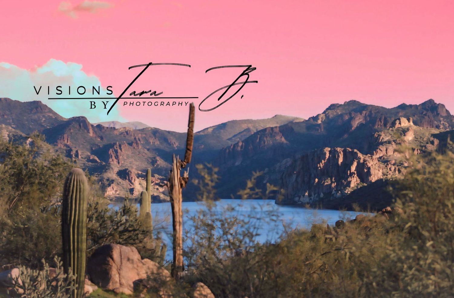 Desert canyon landscape with tall saguaros, rocky cliffs, and warm sunset tones overlooking a shimmering lake below.