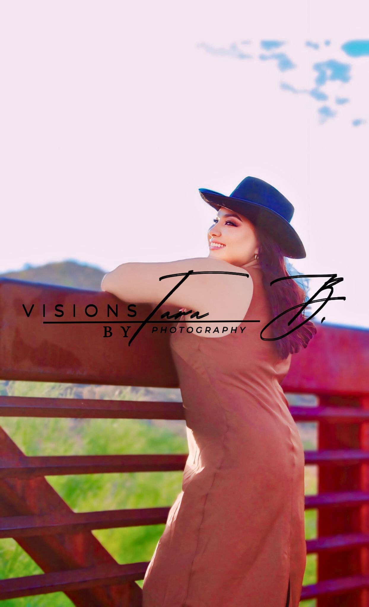 Woman in a cowgirl hat leaning on a wooden fence at sunset, bathed in warm western light with soft desert hues.