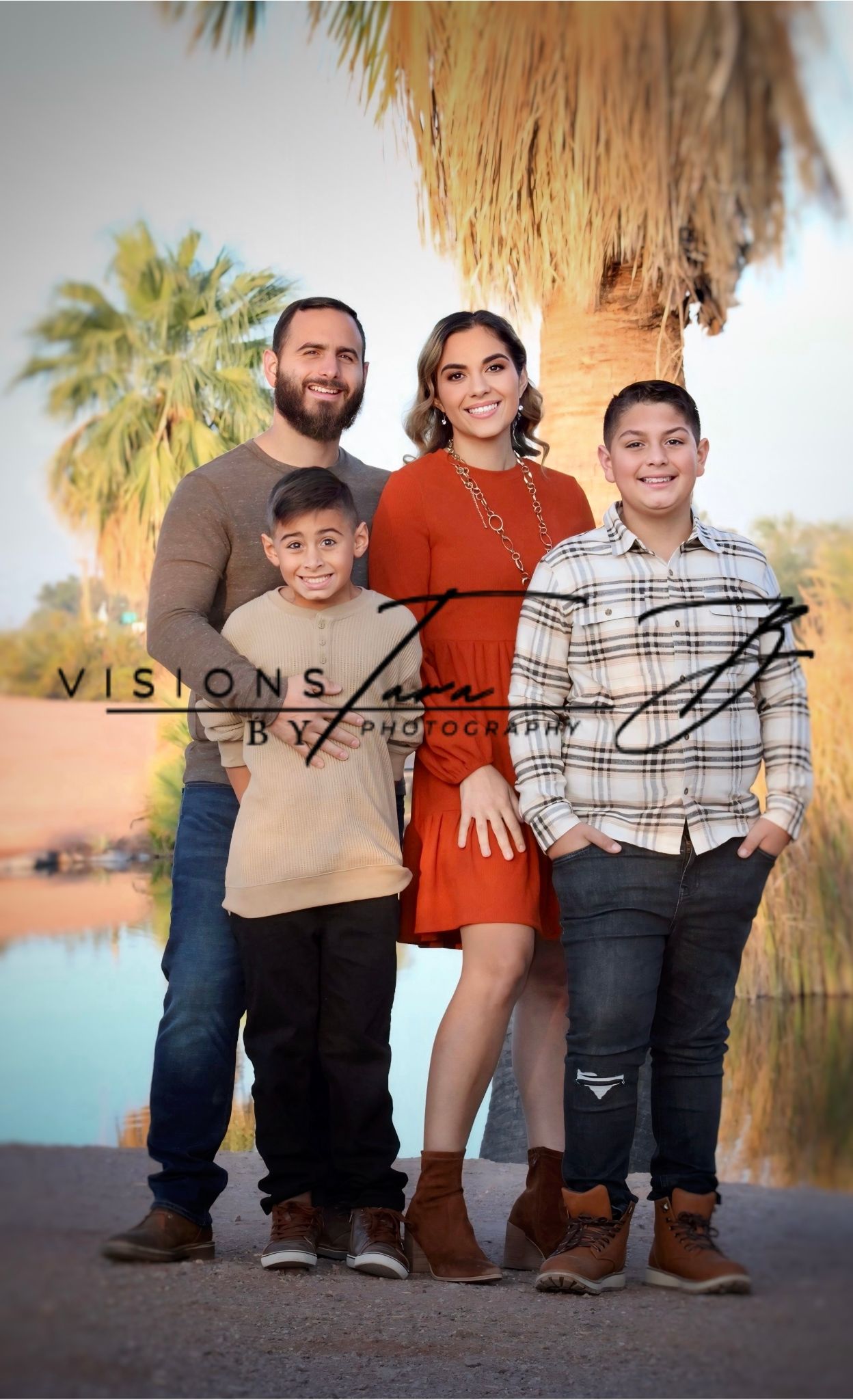 Family portrait of three people smiling outdoors, standing together in front of desert plants and warm natural light.