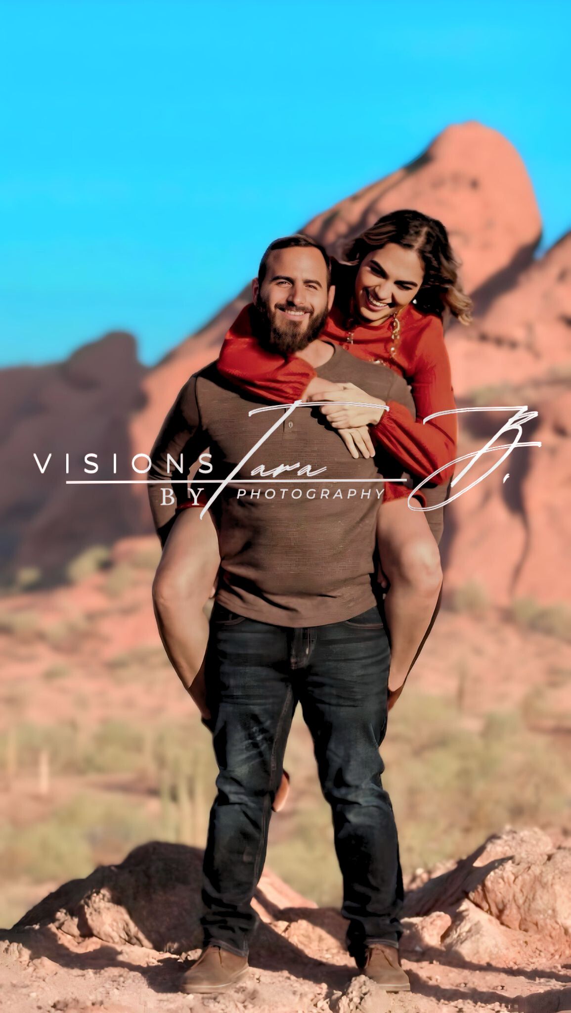 Couple sharing a playful moment in the desert, posing together with bright blue sky and red rock formations behind them.