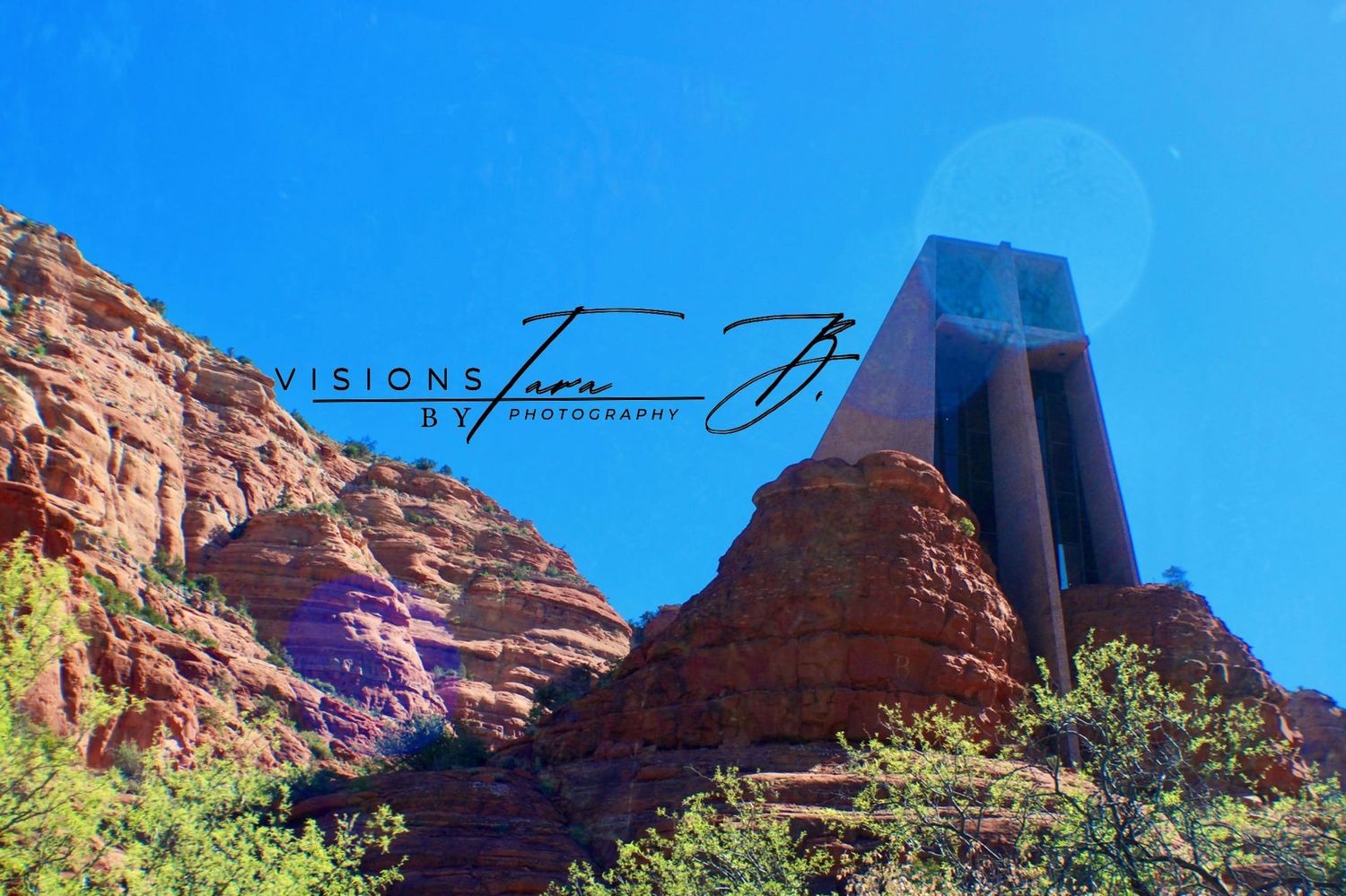 Red rock cliffs in Sedona with bright blue sky and sun flare, featuring the Chapel of the Holy Cross emerging from the hillside.
